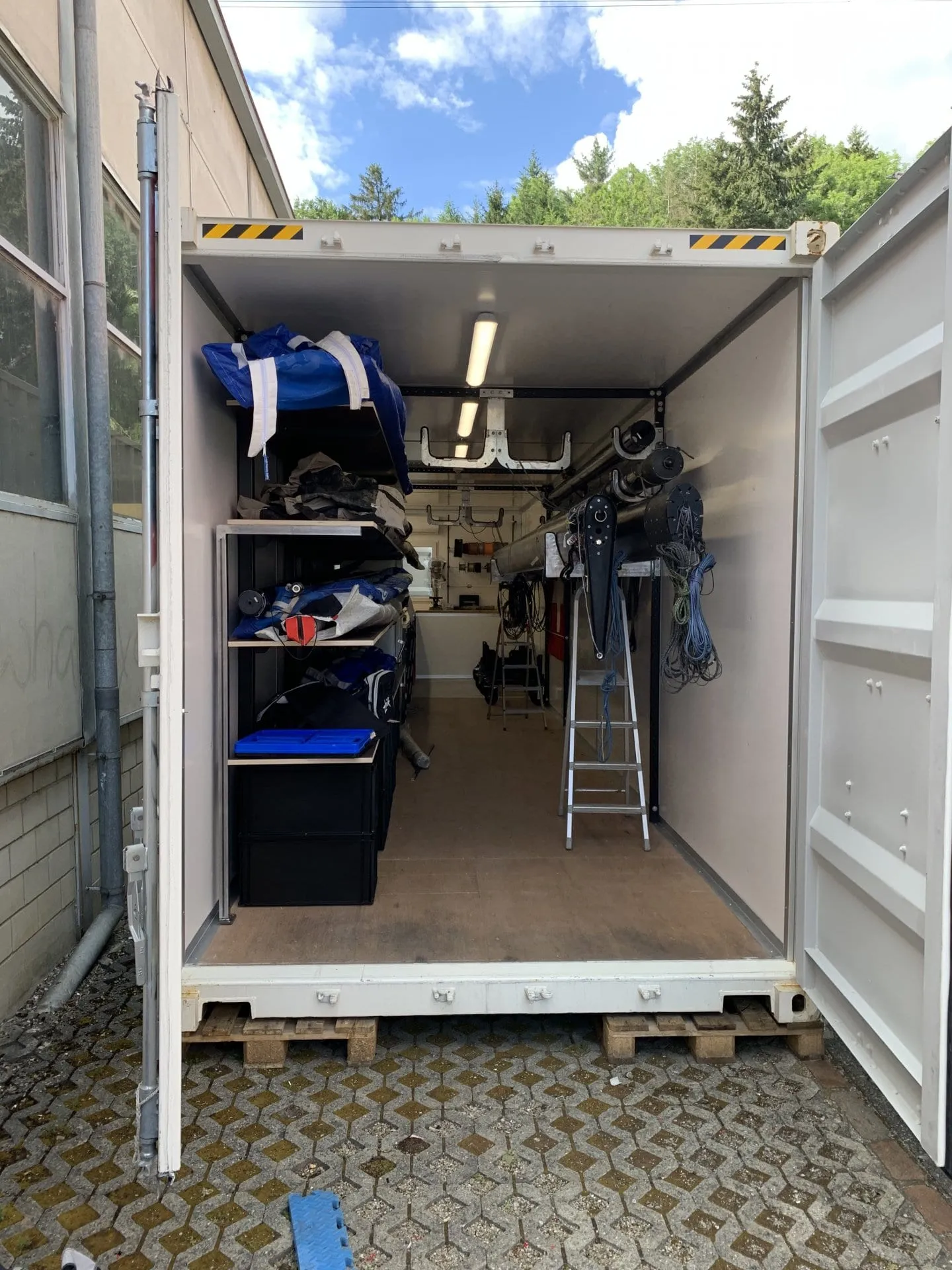Geöffneter Container mit Regalen voller Segelsäcke, Mast auf Haltern, Leiter und Tauwerk
