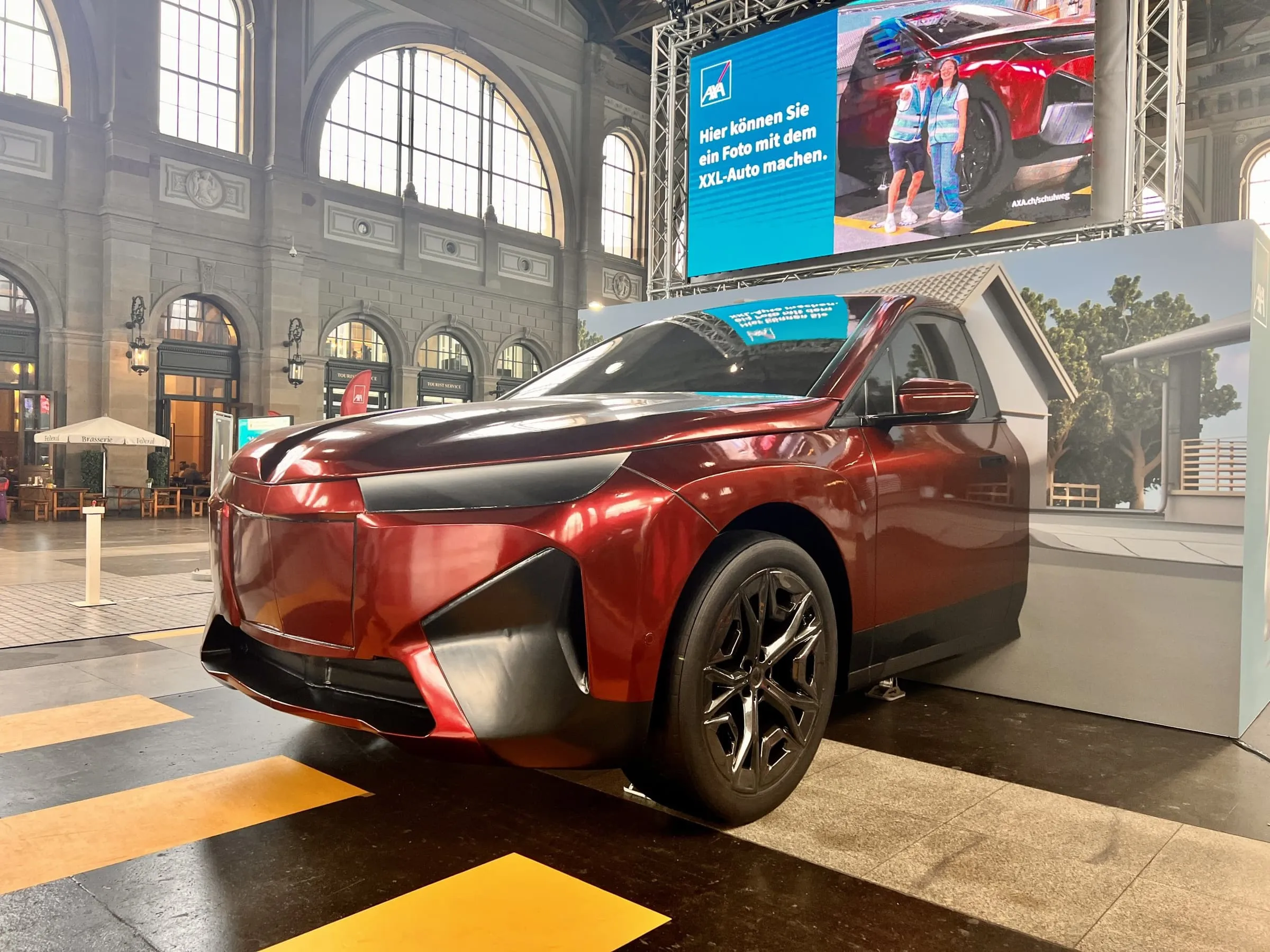 Oversized red XXL car from AXA in the concourse of Zürich main station, an LED screen behind it