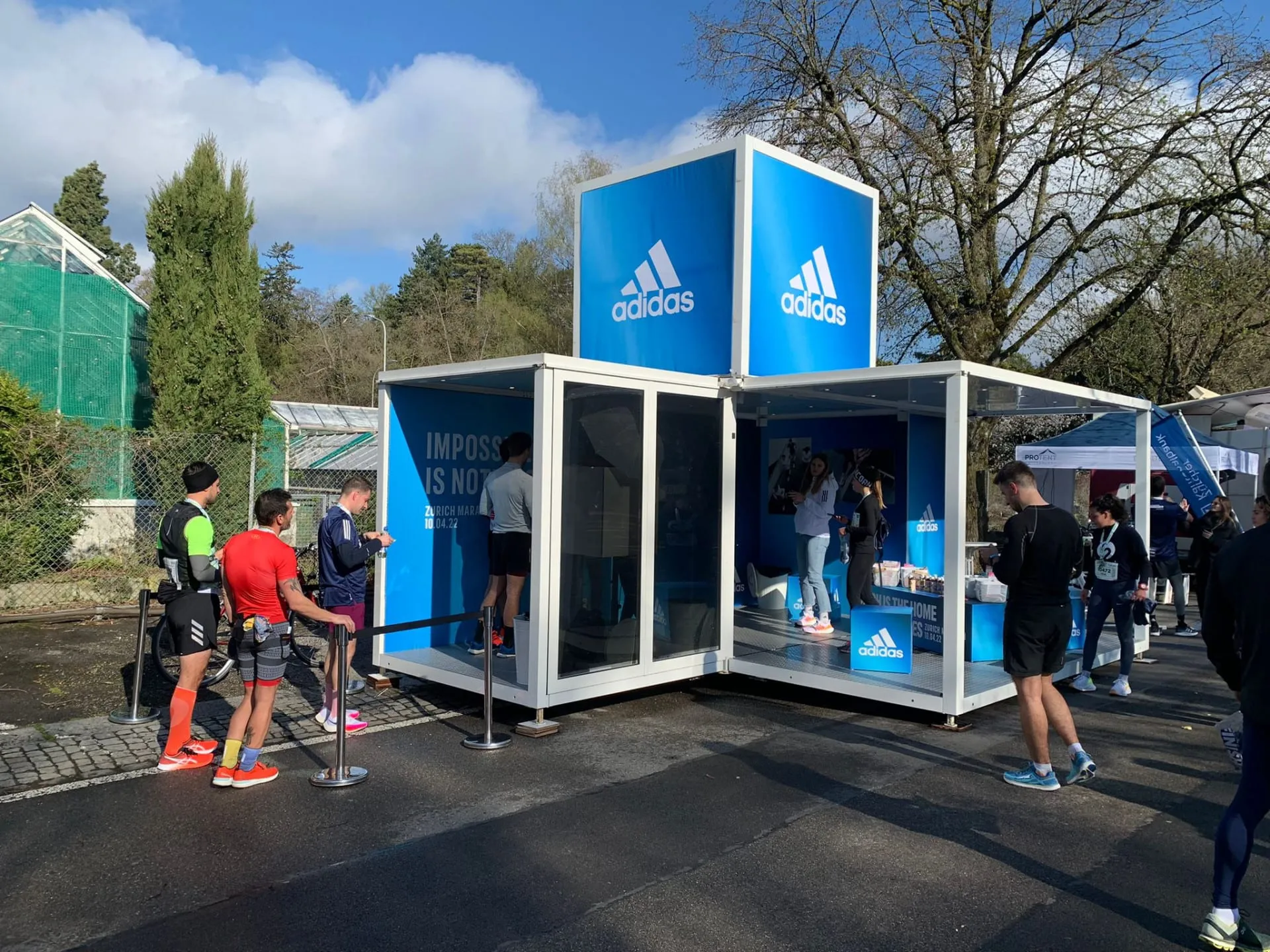 Runners waiting outside the blue-and-white adidas Promocube with glass walls and an adidas cube on the roof