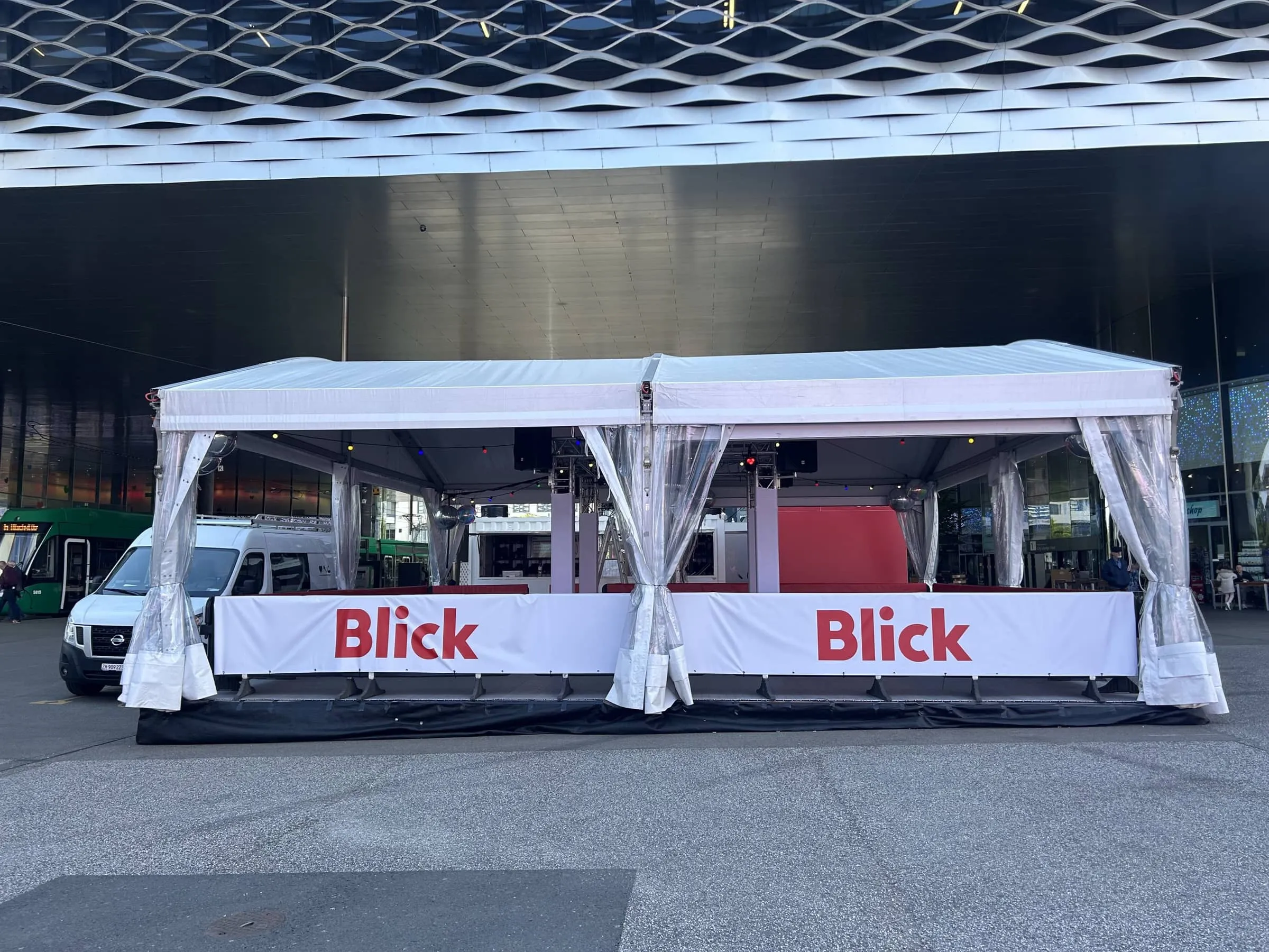 Leeres Blick-Zelt mit weissem Dach, Blick-Banden und Traversen vor der Messe Basel, links ein weisser Lieferwagen
