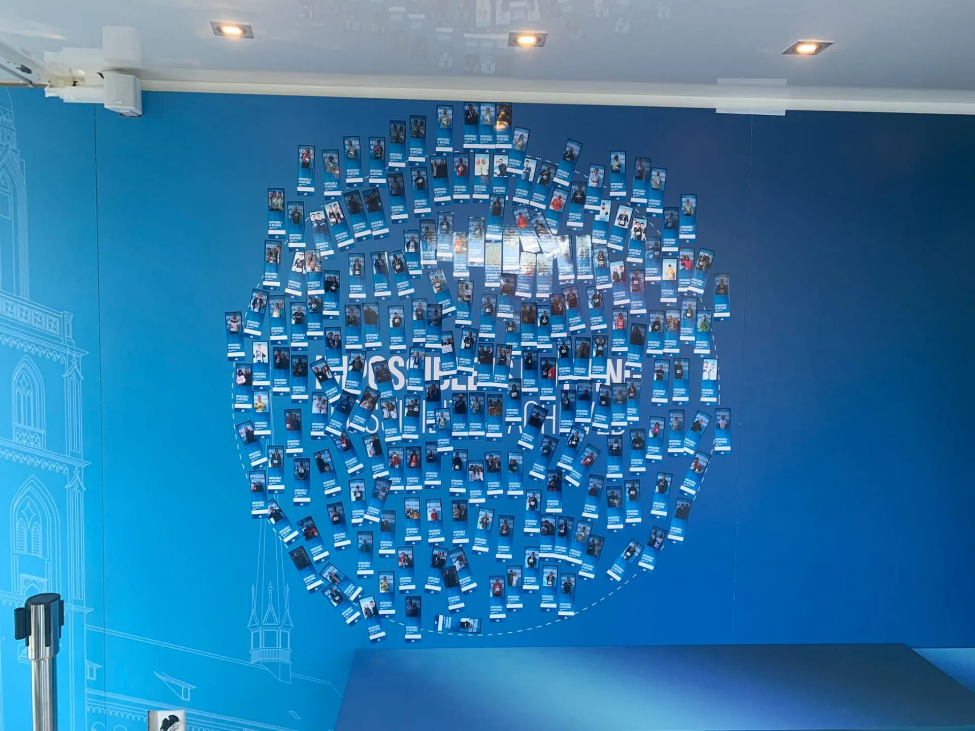 Kreisförmige Collage aus vielen Fotostreifen an blauer Wand mit Schriftzug Impossible is Nothing