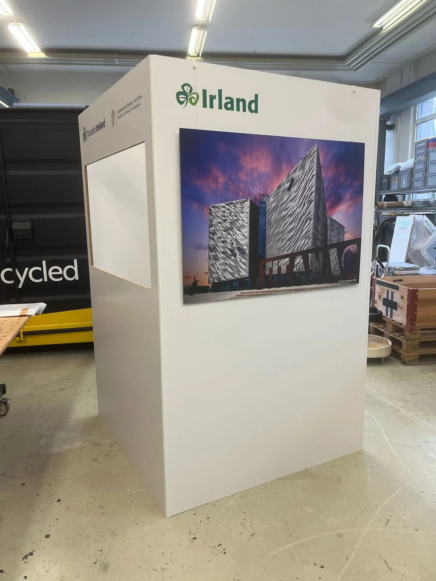 Gefaltete Stellwand mit zwei Küstenfotos und Irland-Logo, davor ein Pappschaf in der Werkstatt