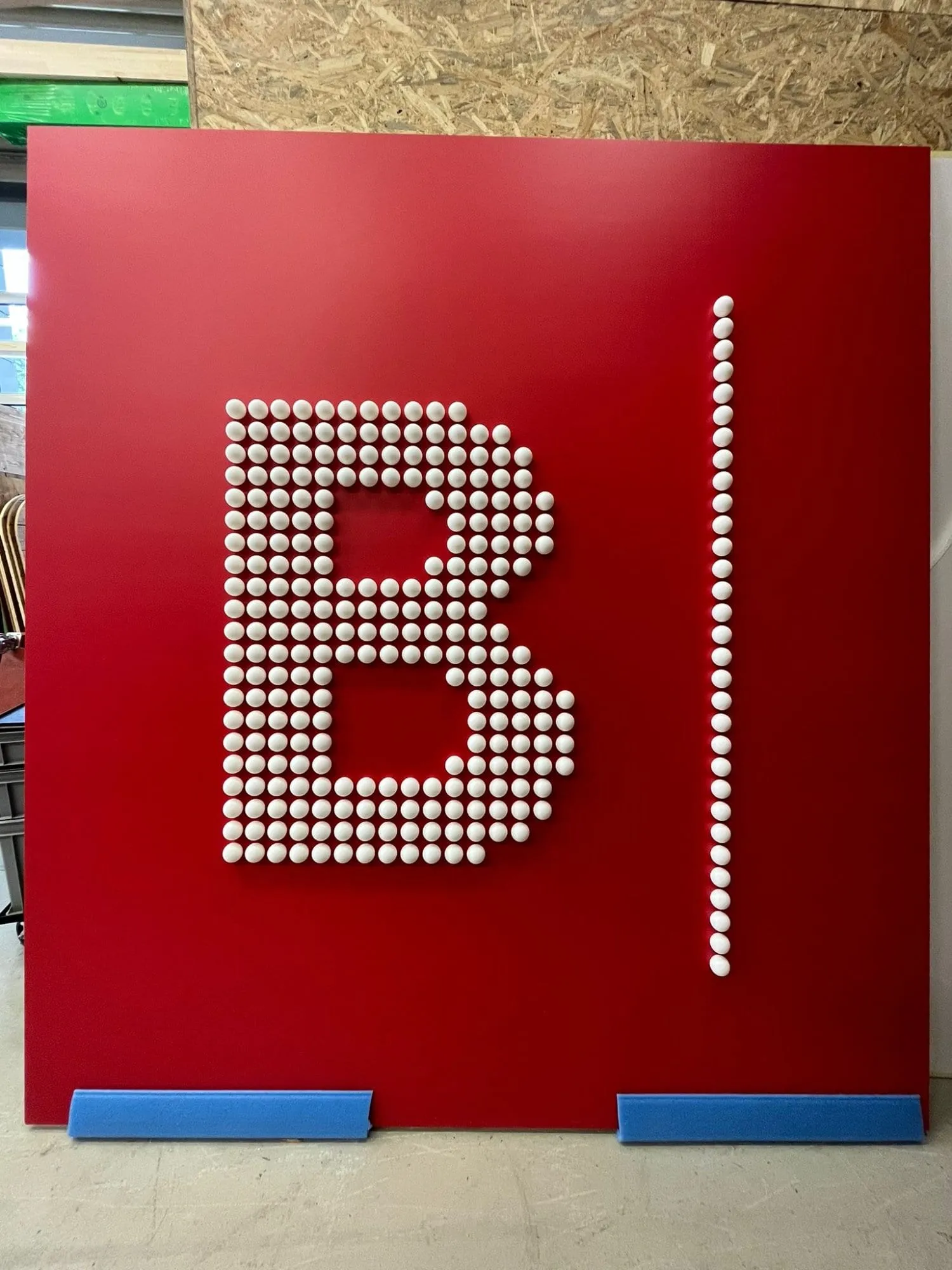 Rote Platte mit dem Buchstaben B und einem Strich aus weissen Tischtennisbällen in der Werkstatt