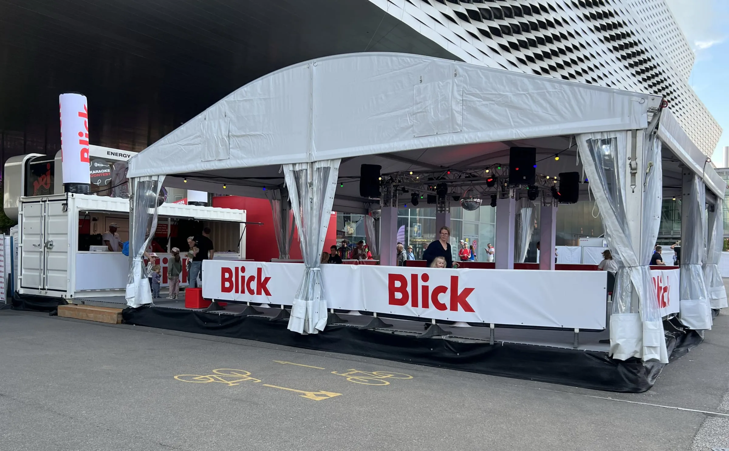 Blick roller disco under a white tent roof with branded barriers, a disco ball and a container outside Messe Basel