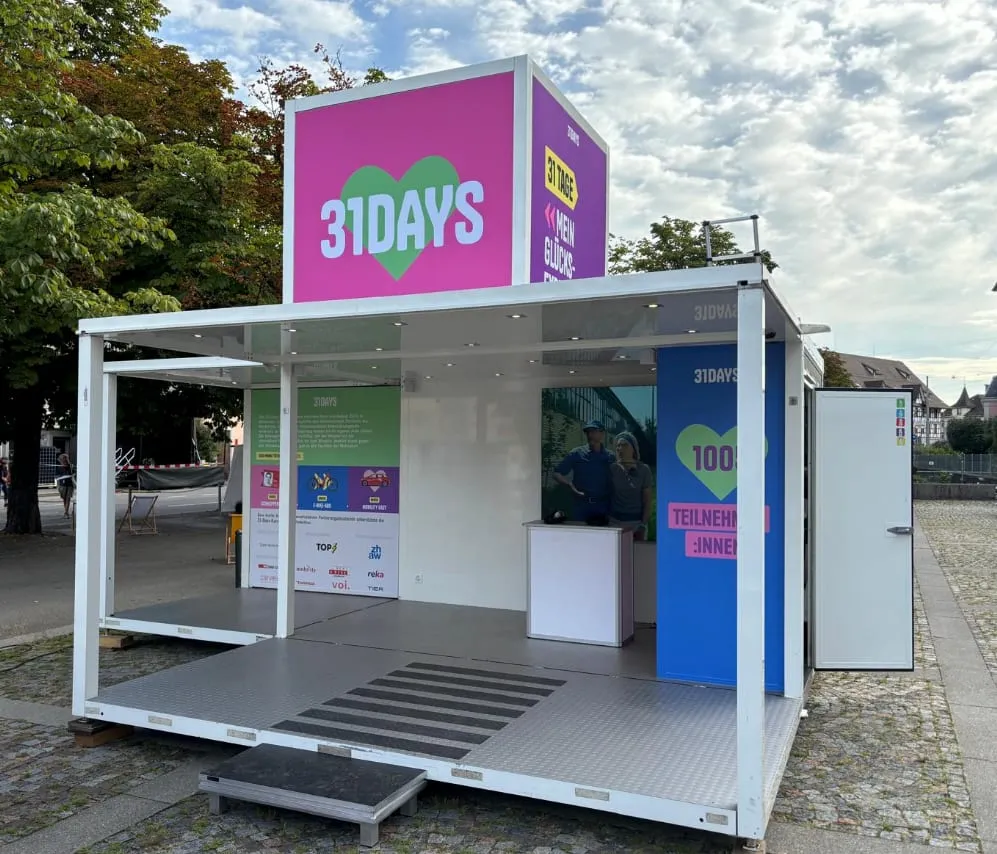 White Promocube with a pink 31DAYS cube on the roof and an open front on a paved square in Winterthur