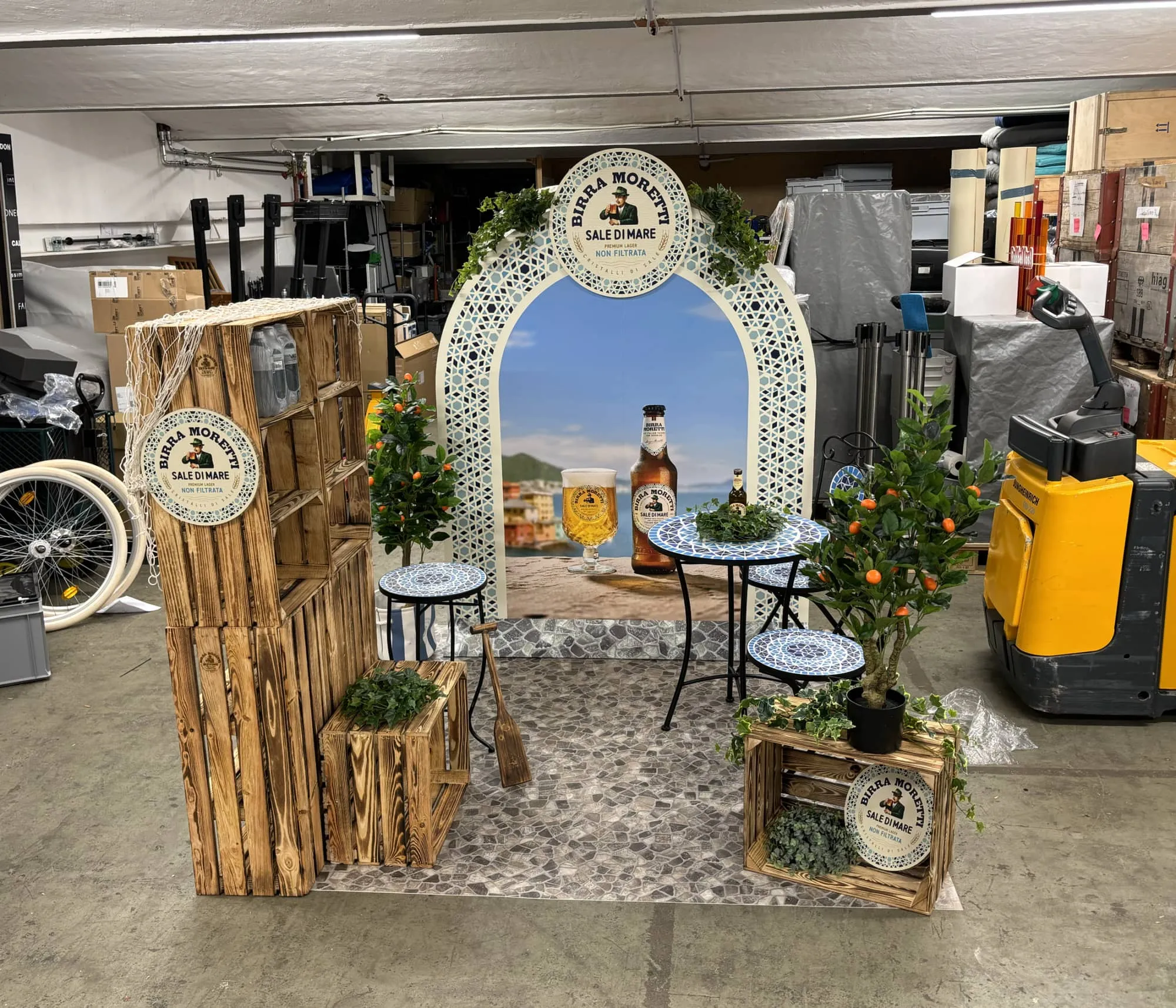 Birra Moretti corner in a warehouse with a mosaic arch, sea image, ceramic tables, wooden crates and small orange trees