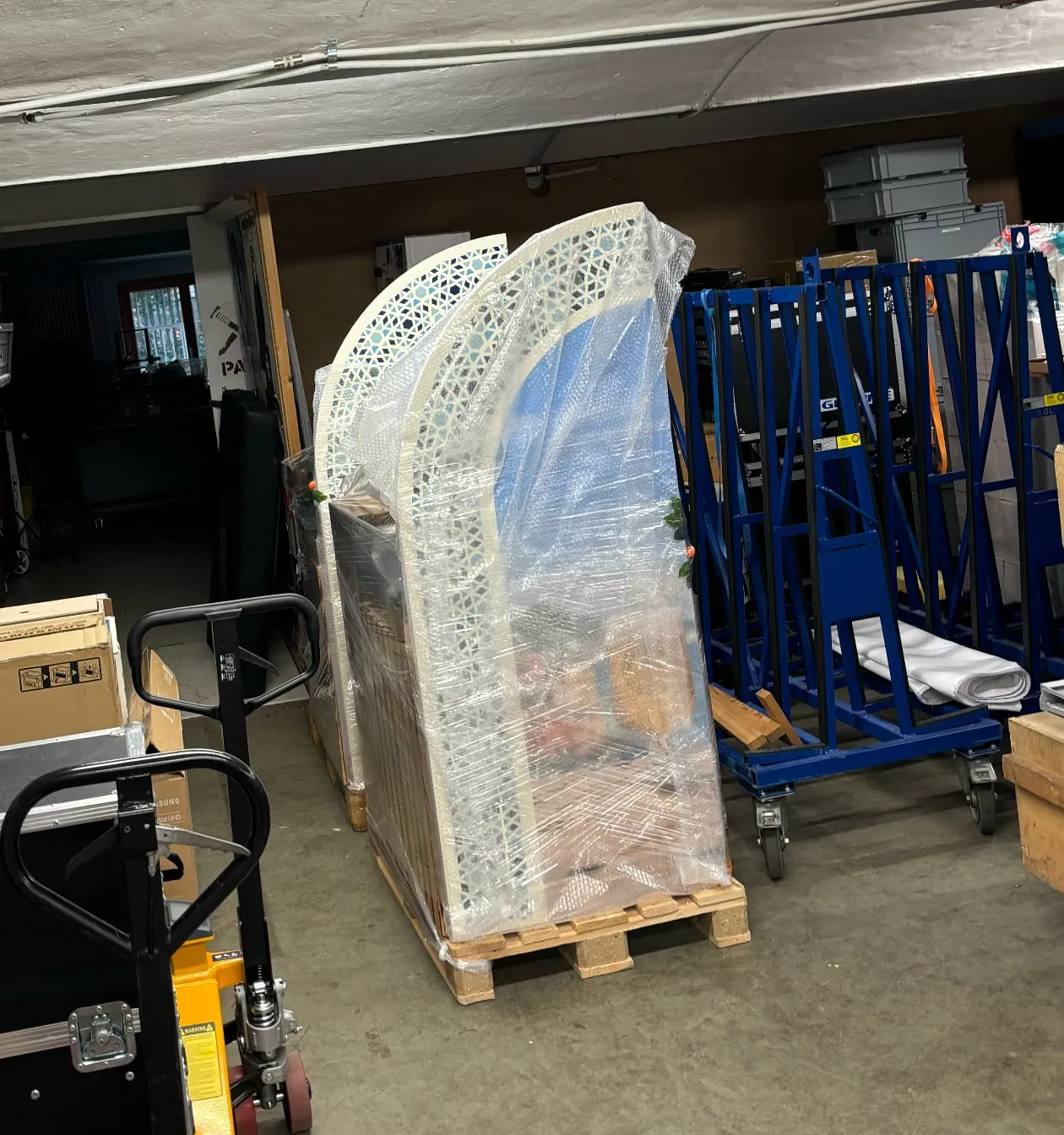 Verpackter Corner auf Palette im Lager, Torbogen in Luftpolsterfolie neben blauen Transportgestellen