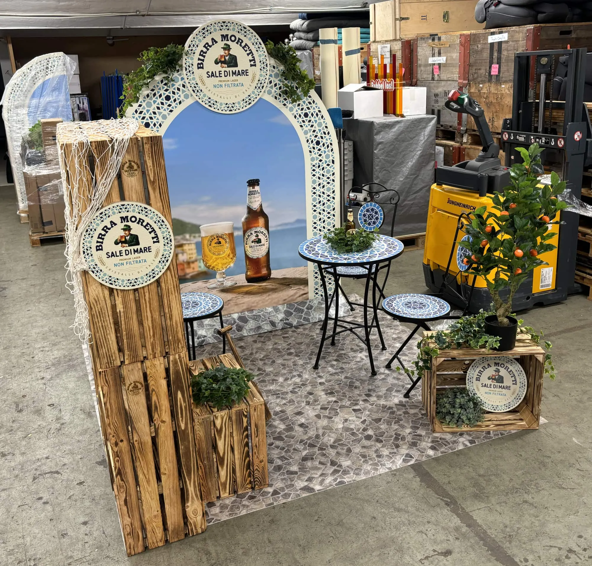 Corner schräg von vorne mit Holzkistenregal, Mosaiktischen und Orangenbäumchen auf dem Steinmosaik-Bodenbelag