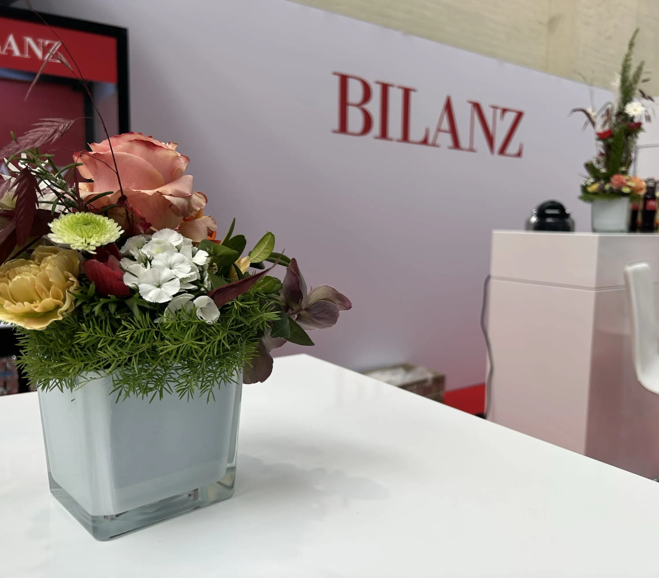 Blumenstrauss in weisser Vase auf Stehtisch, dahinter das rote BILANZ-Logo an der weissen Standwand
