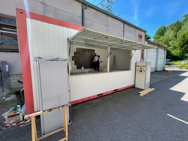 Rot-weisser Container mit geöffneter Klappe vor Industriehalle, innen wird an einer Wand gearbeitet