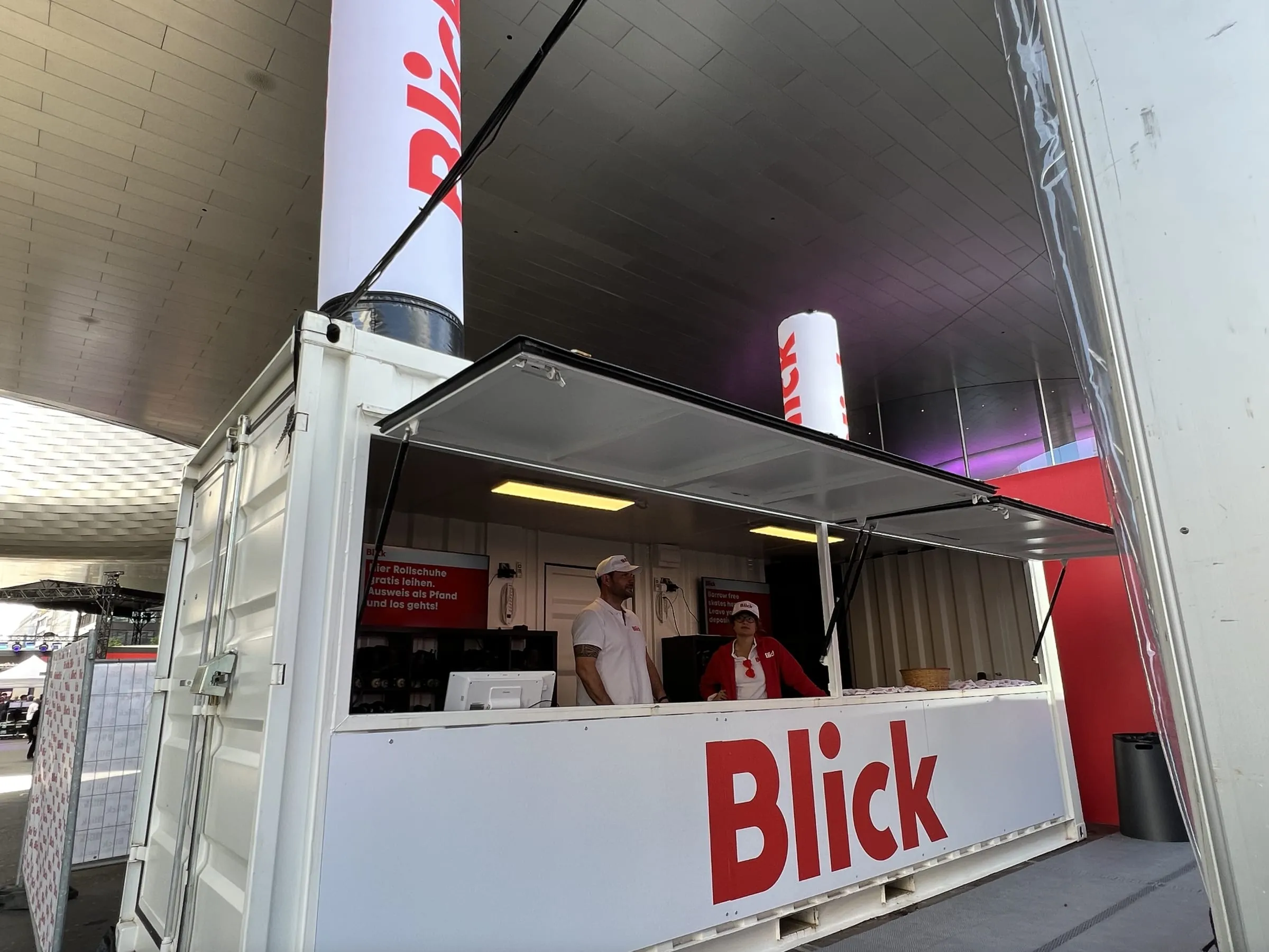 Weisser Blick-Container mit hochgeklappter Front, zwei Promotor an der Theke und Blick-Säule auf dem Dach