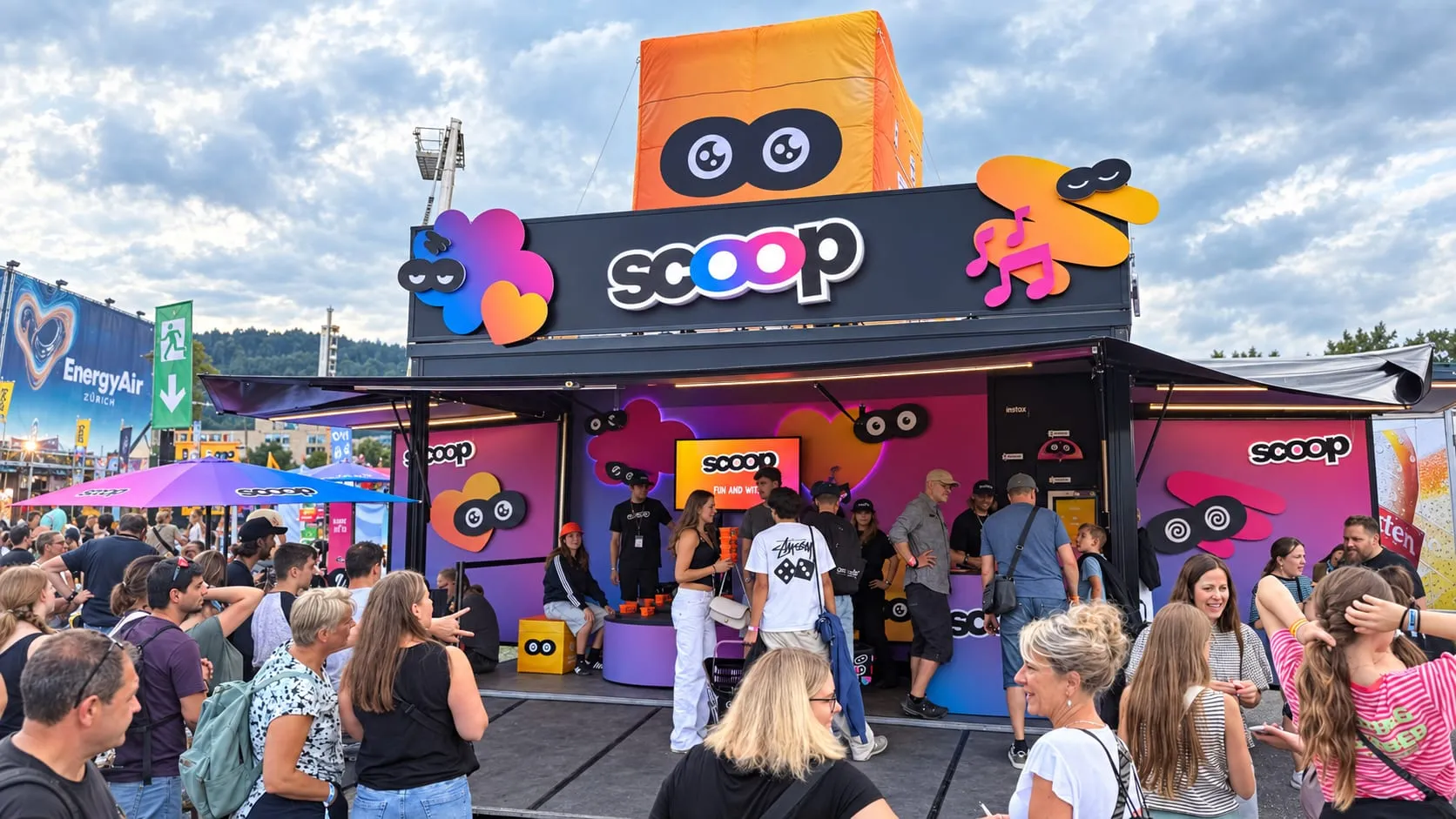Festival visitors in front of the scoop container with a stage, a screen and eye emojis, an Energy Air banner on the left