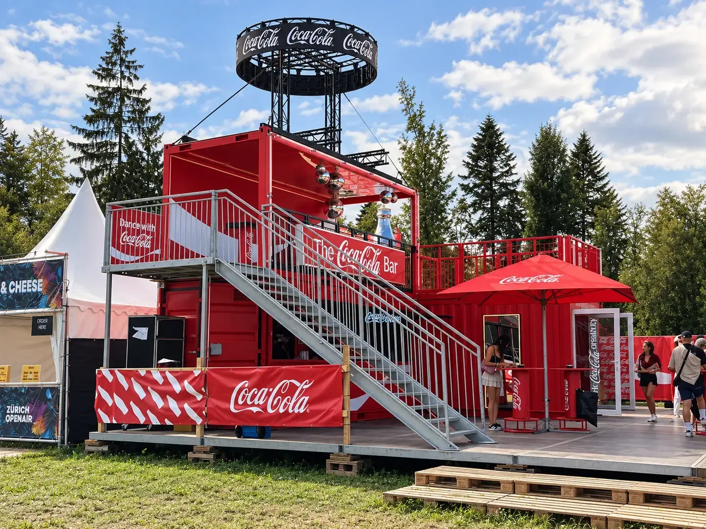 Rote Coca-Cola-Bar aus zwei gestapelten Containern mit Aussentreppe, Dachterrasse, Sonnenschirm und Truss-Ring am Zürich Openair