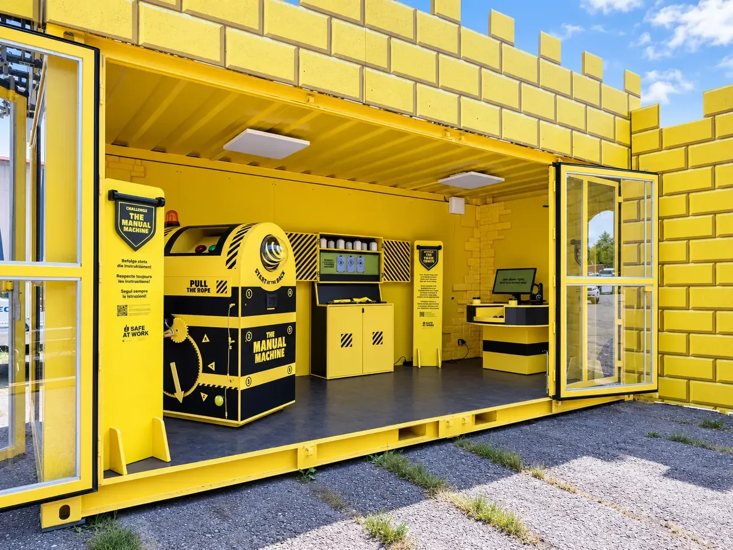 Gelber Container mit Zinnen-Fassade und geöffneter Seite, drinnen die schwarz-gelbe Station «The Manual Machine» mit Seilzug und Warnleuchte