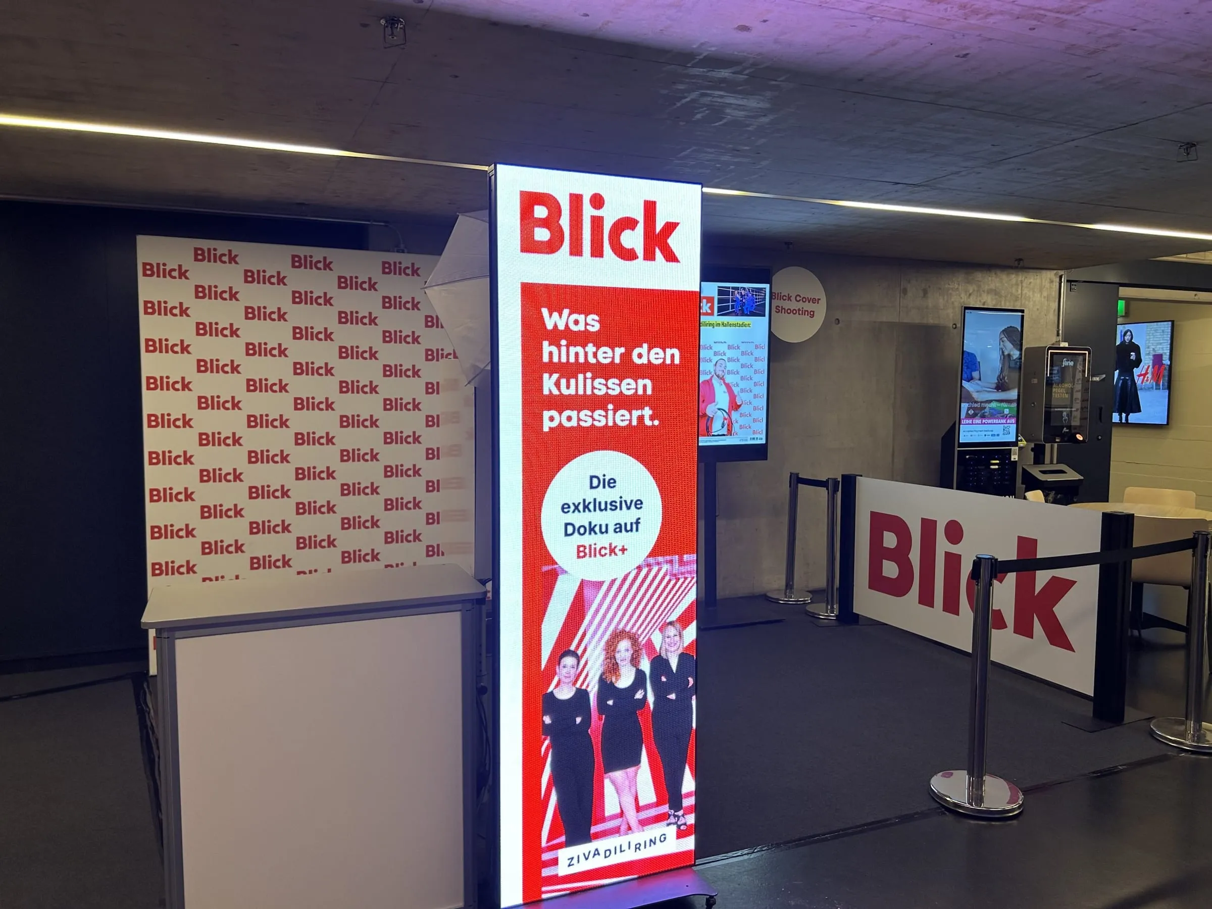 Leuchtende Blick-Stele mit Zivadiliring-Doku-Werbung, daneben Blick-Logowand und Absperrbanner