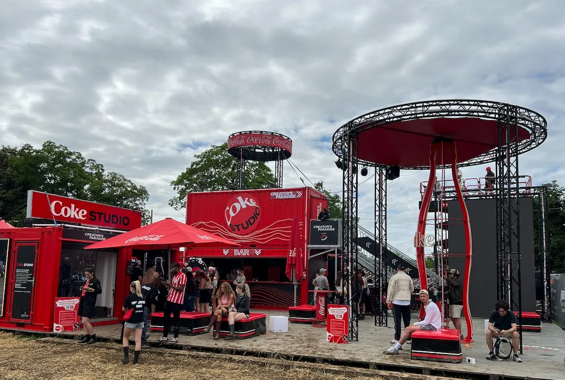 Coke Studio area built from red containers with a bar, a round truss tower and visitors on seating cubes