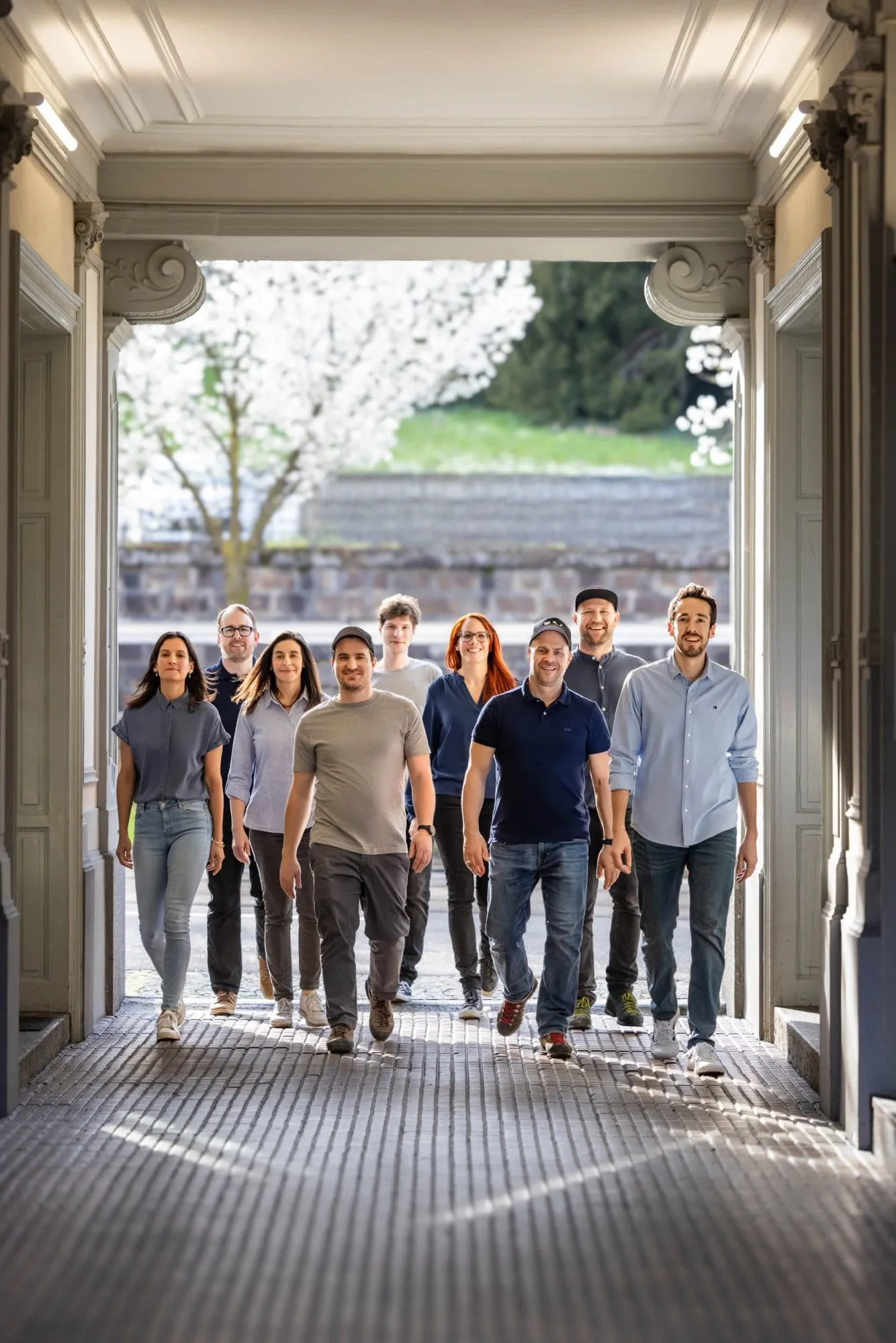 Nine team members walking through a bright archway with a blossoming tree in the background