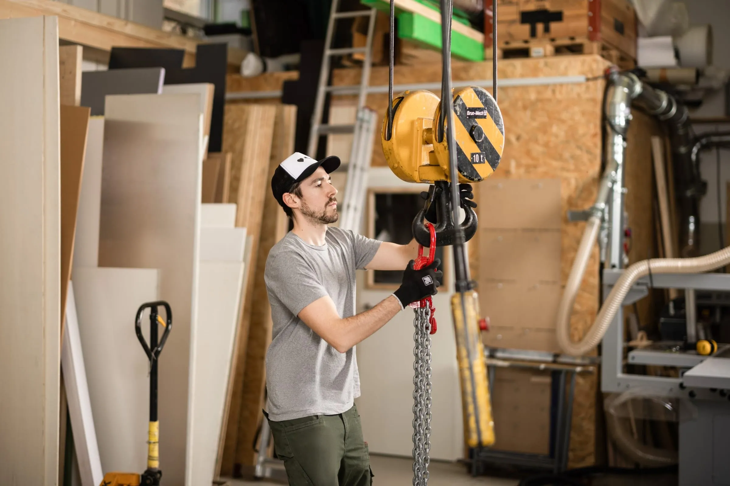 Man in a cap and gloves hooking a chain into a yellow 10-tonne hall crane