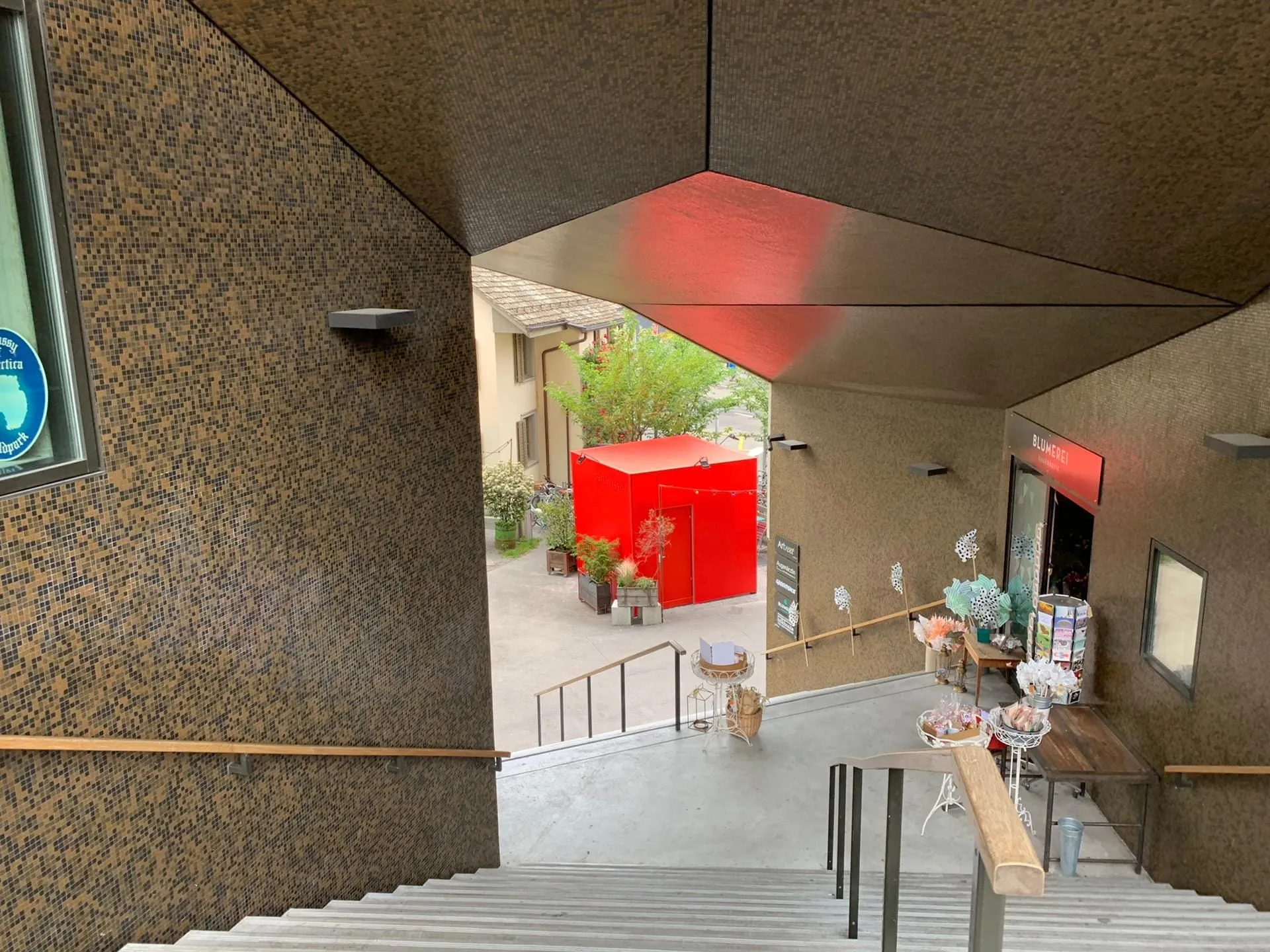 Roter Cube in einem Innenhof mit Velos und Pflanzen, gesehen von einer Treppe aus