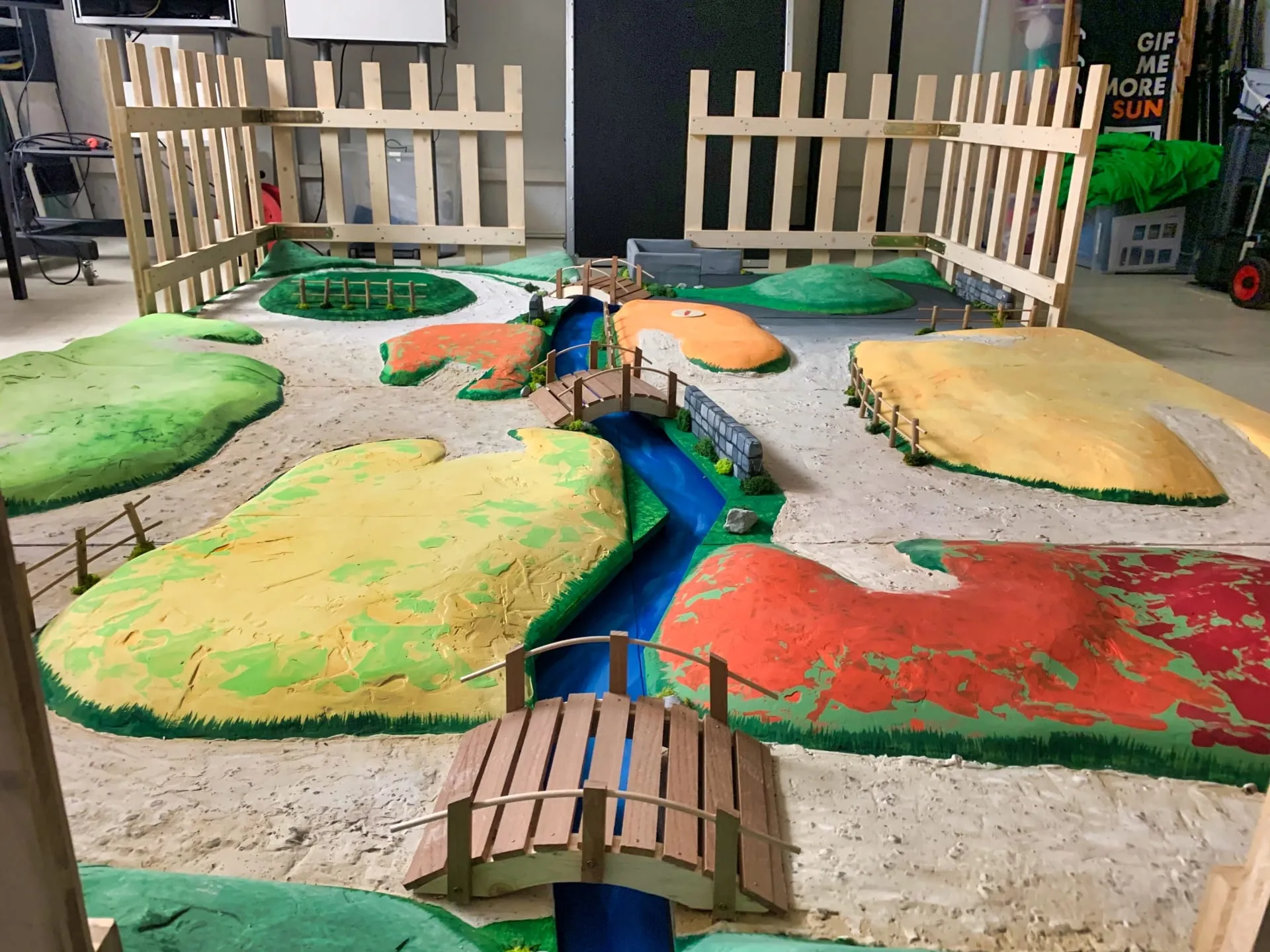 Handgefertigte Modelllandschaft mit bunten Feldern, blauem Fluss, Holzbrücken und Zäunen in der Werkstatt
