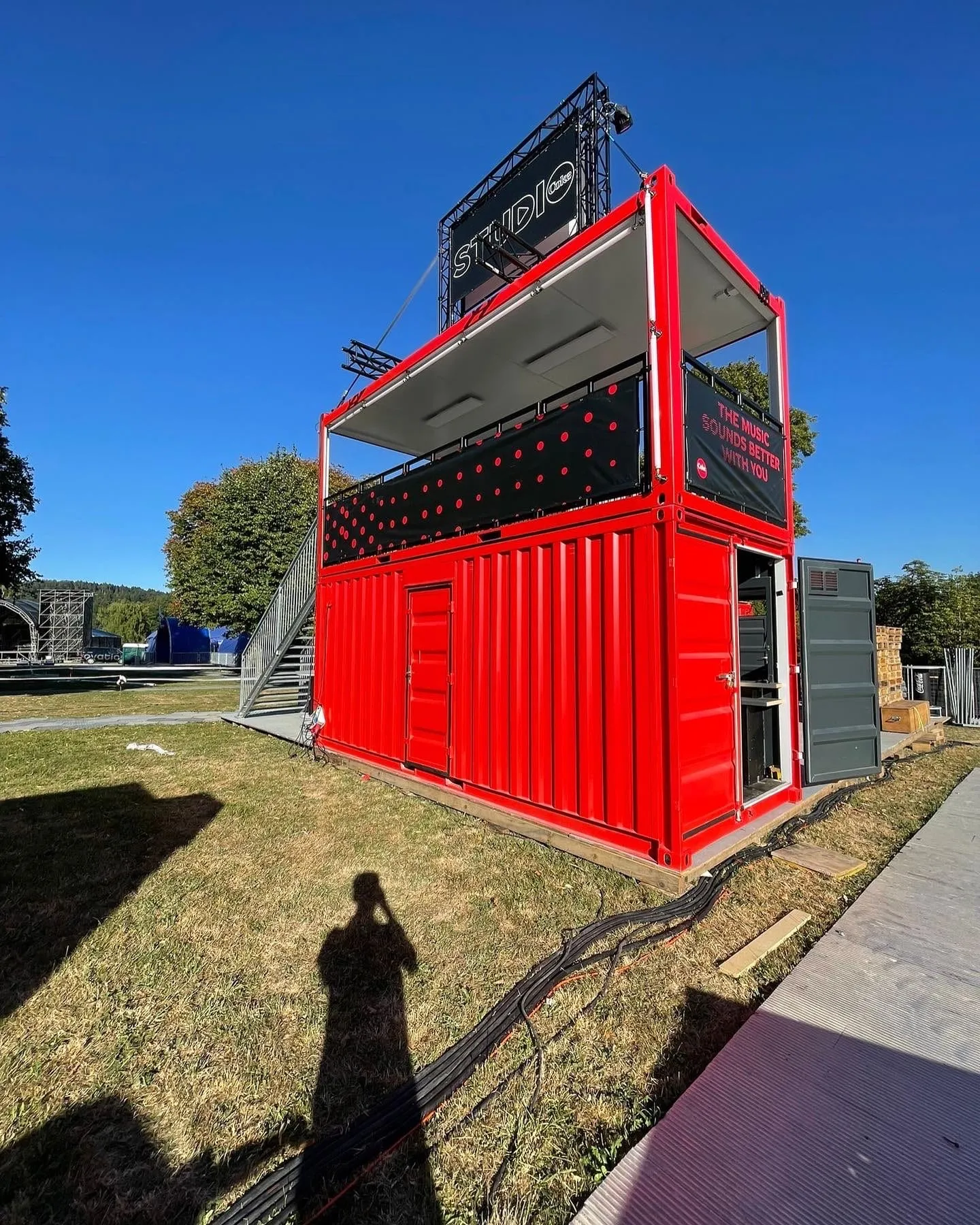 Roter Doppelcontainer mit Terrasse, gepunktetem Banner und Coke-Studio-Schild auf dem Festivalgelände