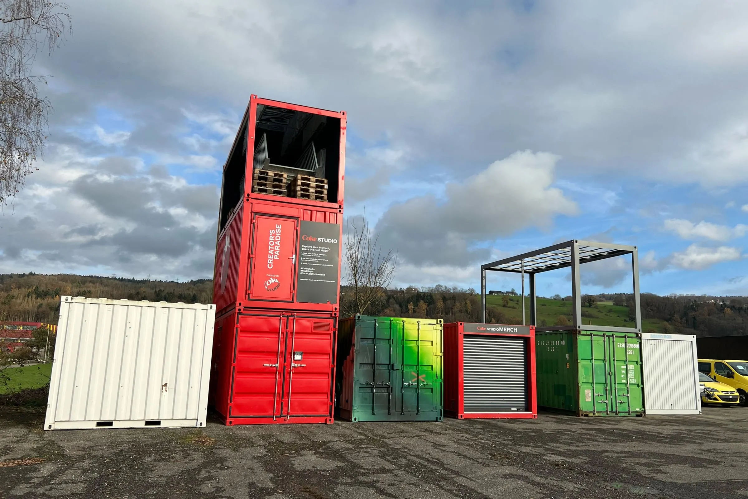 Stacked red Coke Studio containers next to green and white containers in an outdoor yard