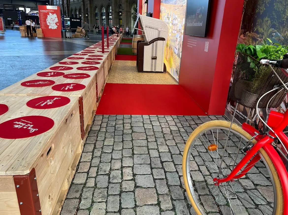 Verschiedene Bodenbeläge aus Pflastersteinen, rotem Teppich und Holz entlang der Bank, rotes Velo im Vordergrund