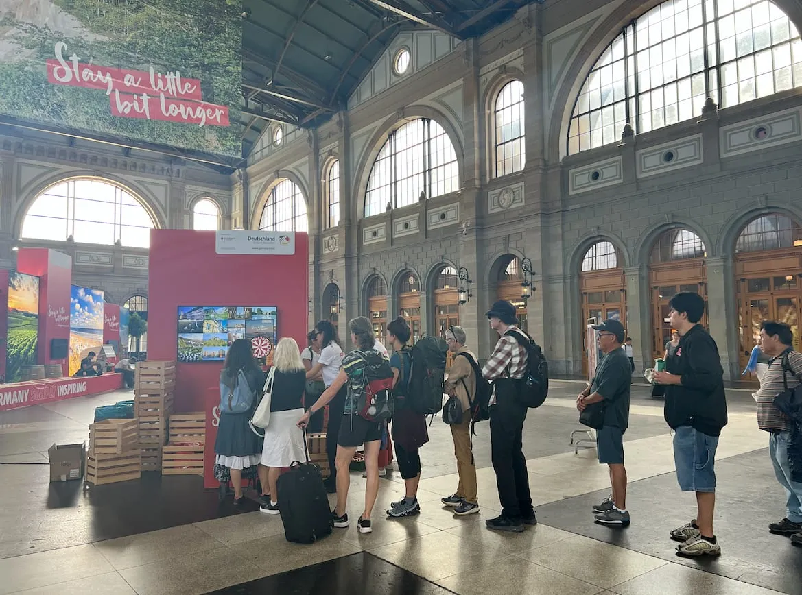 Warteschlange von Passant vor dem Bildschirm mit dem digitalen Glücksrad in der Bahnhofshalle