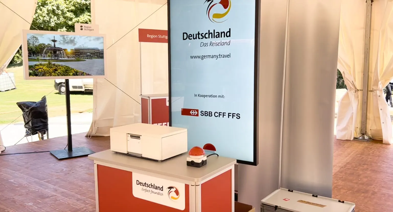 Reiseideen-Generator mit Bondrucker und rotem Buzzer auf roter Theke, daneben Bildschirm «Deutschland Das Reiseland» mit SBB-Logo
