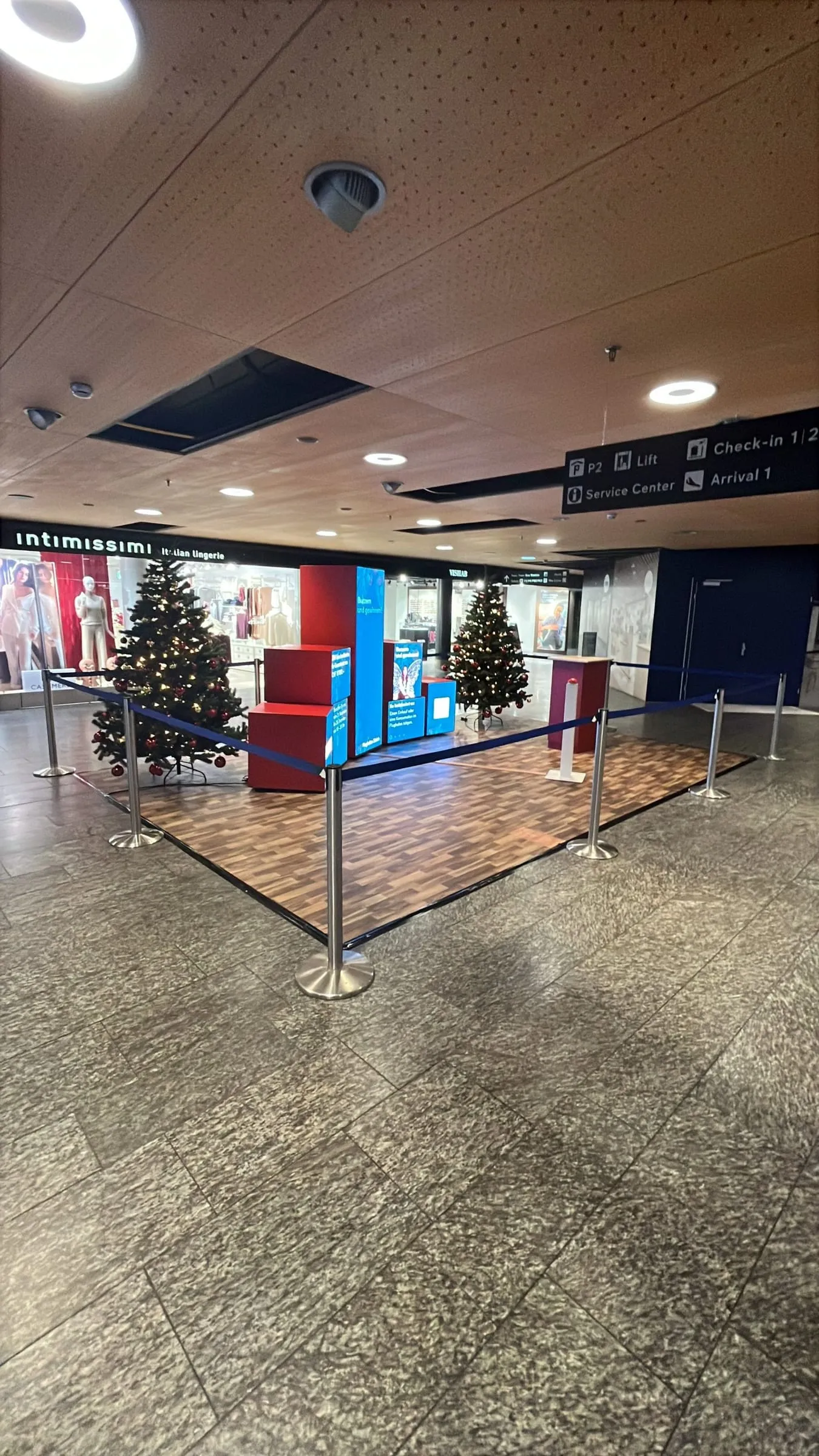 Abgesperrte Aktionsfläche mit Holzboden, roten Kuben, blauem Screen und zwei Weihnachtsbäumen vor dem Intimissimi-Shop