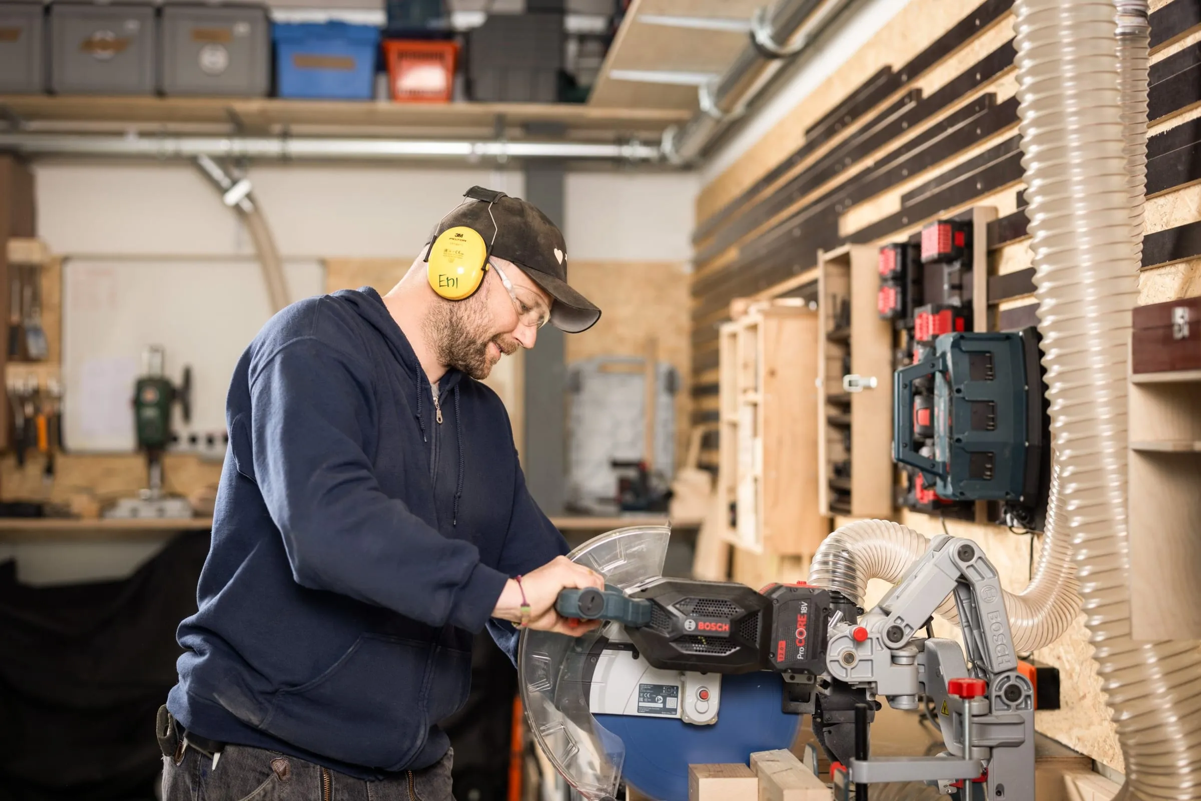 Man in yellow ear defenders and safety glasses cutting wood with a Bosch mitre saw