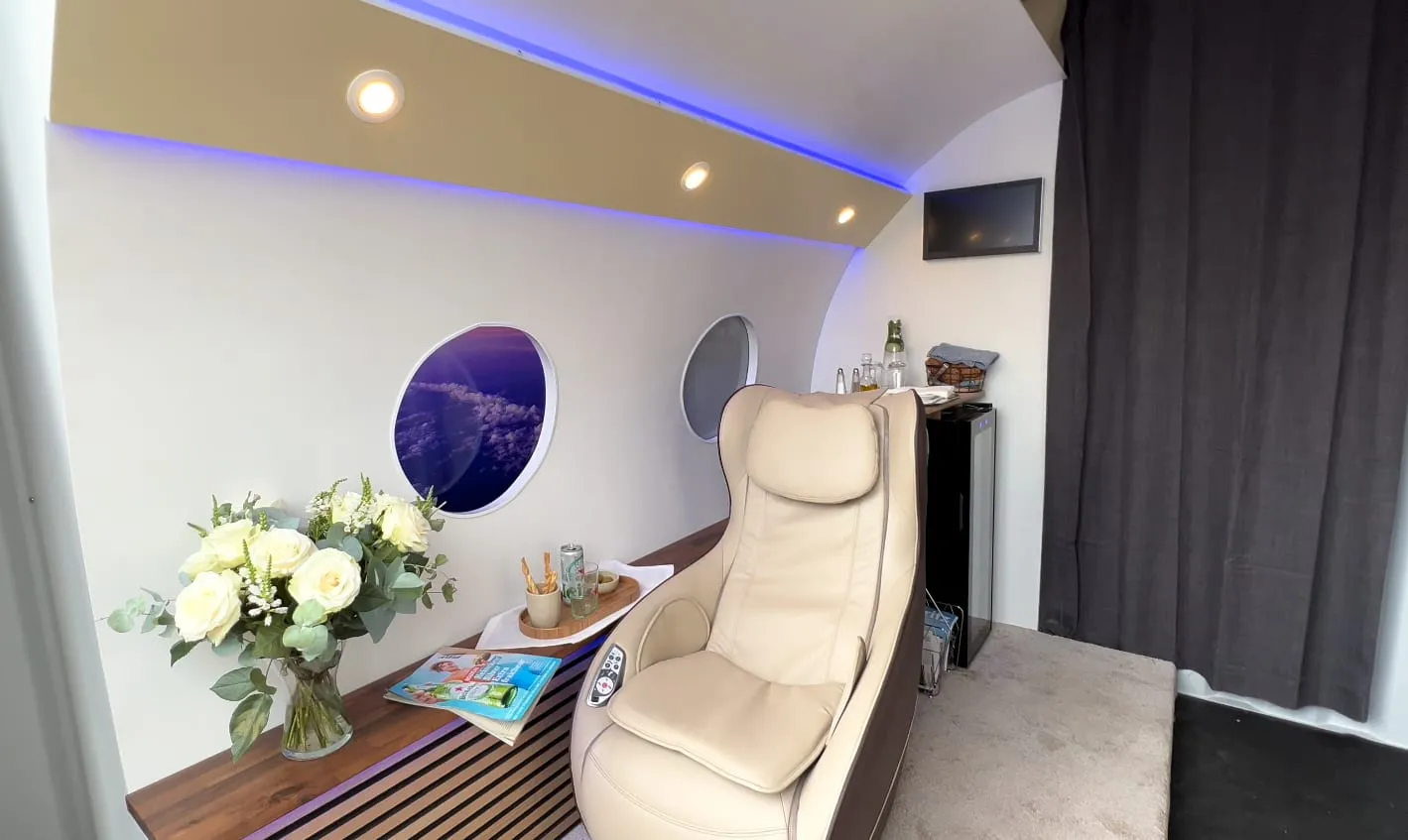 Innenraum der Privat-Jet-Installation mit Massagesessel, Bullaugen, Blumenstrauss, Minibar und violettem LED-Licht