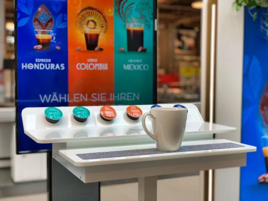 White cup on a rail in front of a screen showing capsules and the Honduras, Colombia and Mexico varieties
