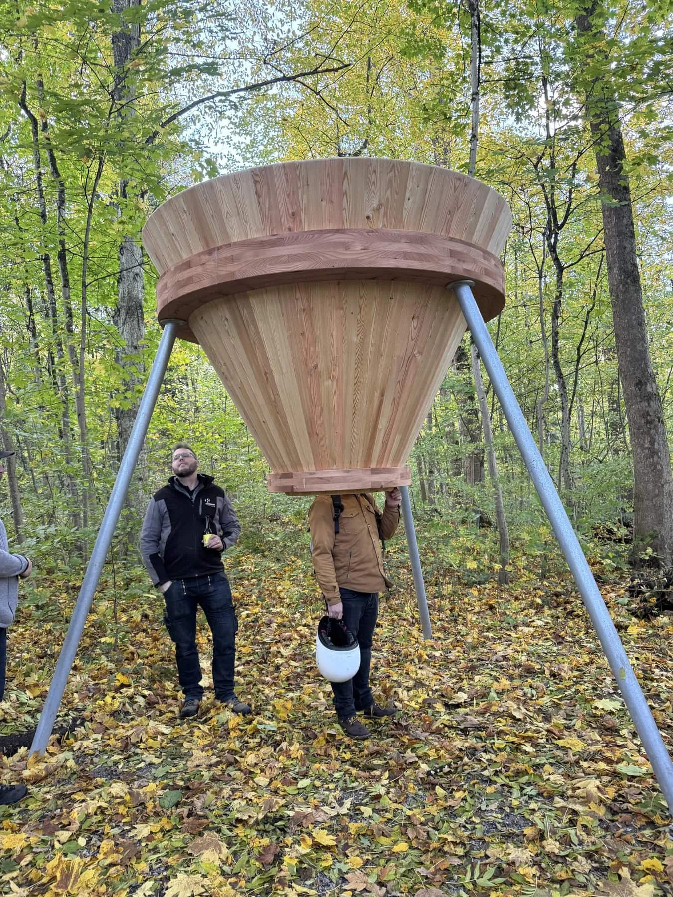 Grosser Holztrichter auf drei Stahlbeinen im Wald, zwei Männer stehen darunter