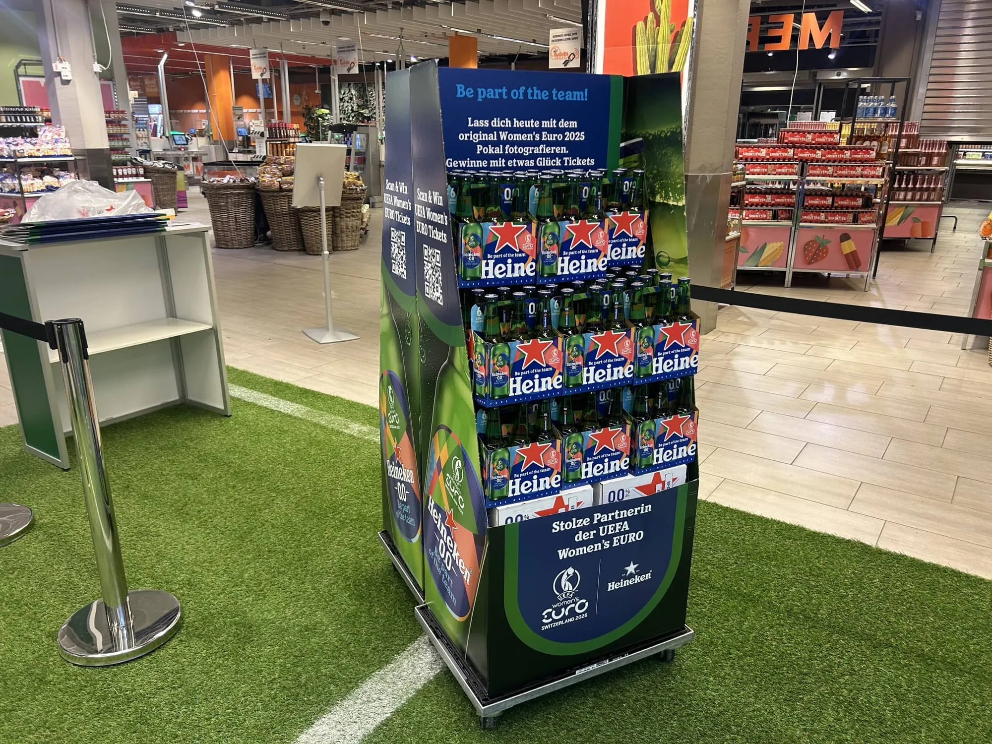 Verkaufsdisplay mit Heineken-0.0-Sixpacks und QR-Code «Scan & Win» auf dem Kunstrasen im Supermarkt