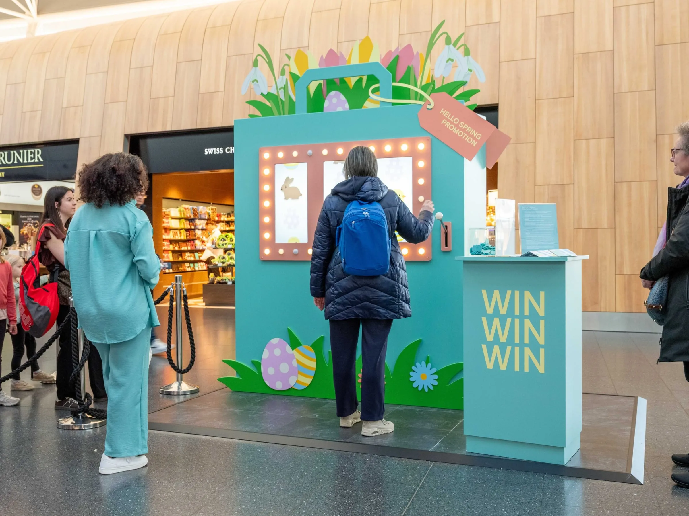 Oversized turquoise shopping-bag set with spring flowers and illuminated frames around three reel windows; a woman pulls the lever beside a «WIN WIN WIN» counter