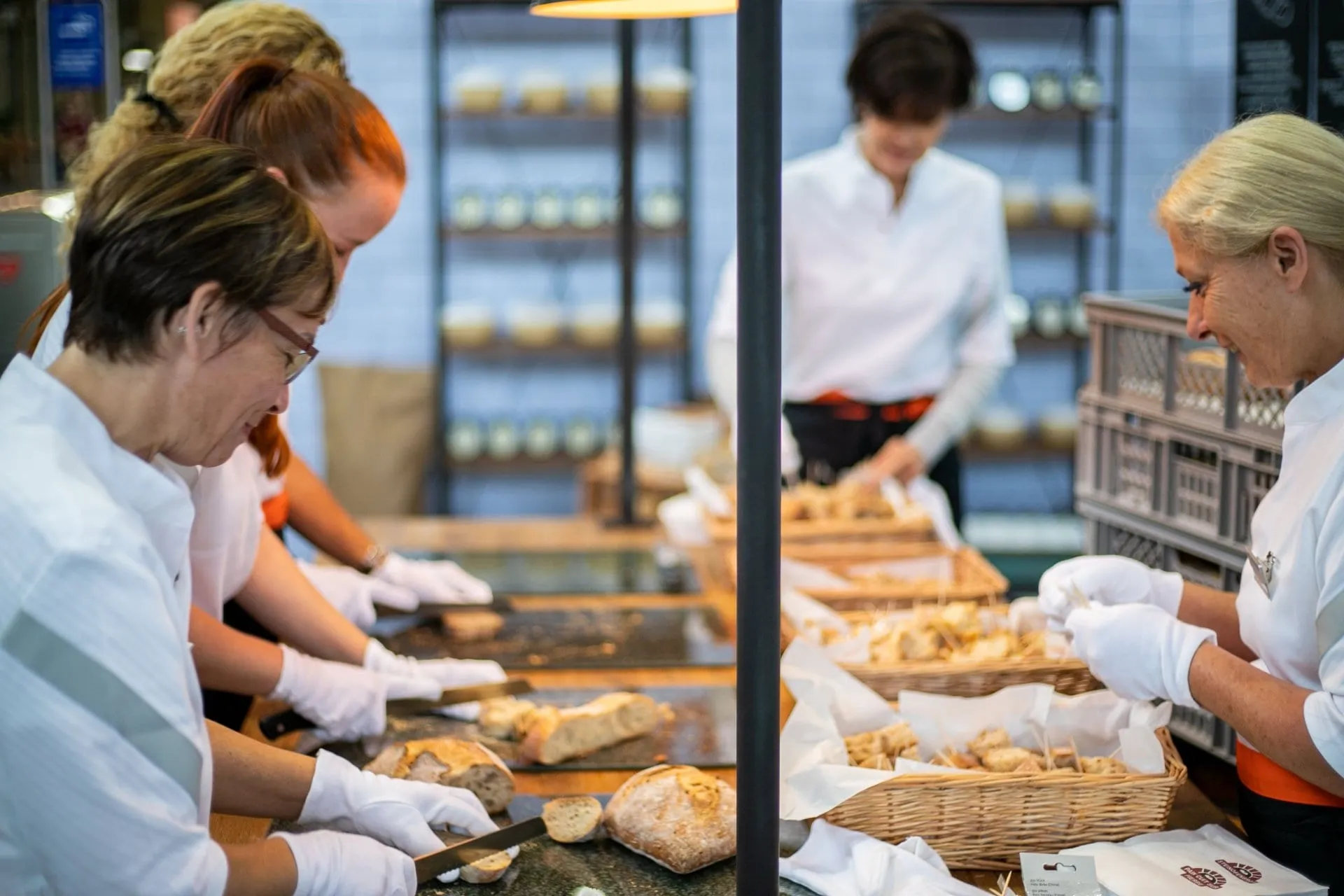 Promotorinnen mit weissen Handschuhen schneiden Brot in Degustationsstücke, Körbe mit Brothäppchen