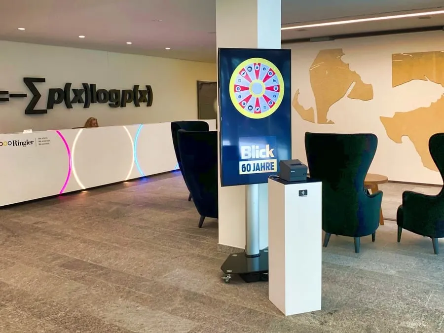 Screen column with a digital Glücksrad and «Blick 60 Jahre» in Ringier's reception hall, beside a badge-reader column