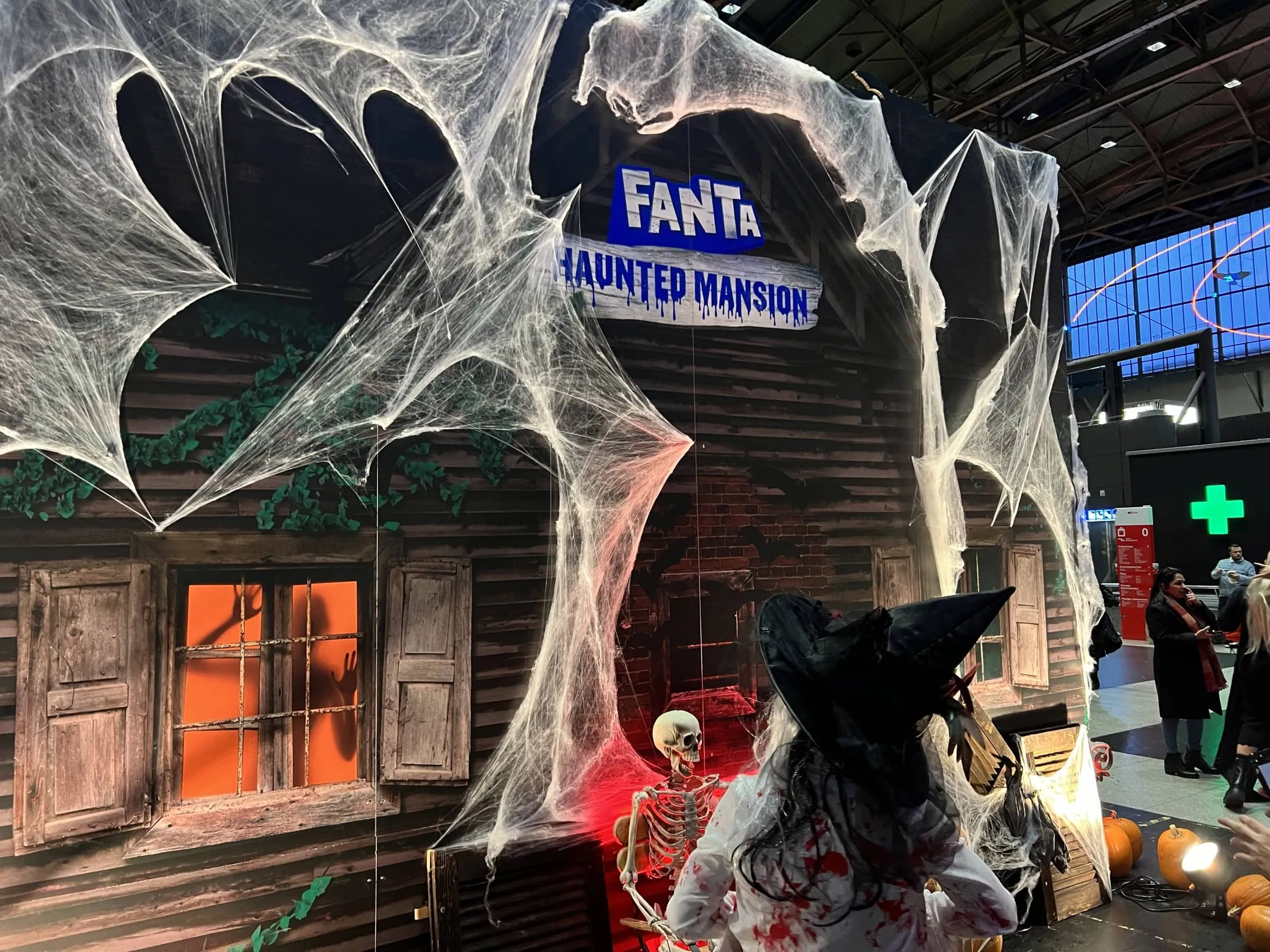 Fassade mit Schild «Fanta Haunted Mansion», Spinnweben, Skelett und eine Person im Hexenkostüm davor