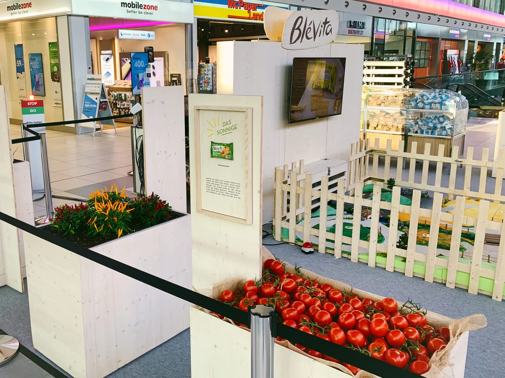 Kiste voller Tomaten, Chili-Pflanzen und Tafel «Das Sonnige» vor dem Zaun der Blévita-Welt im Einkaufszentrum