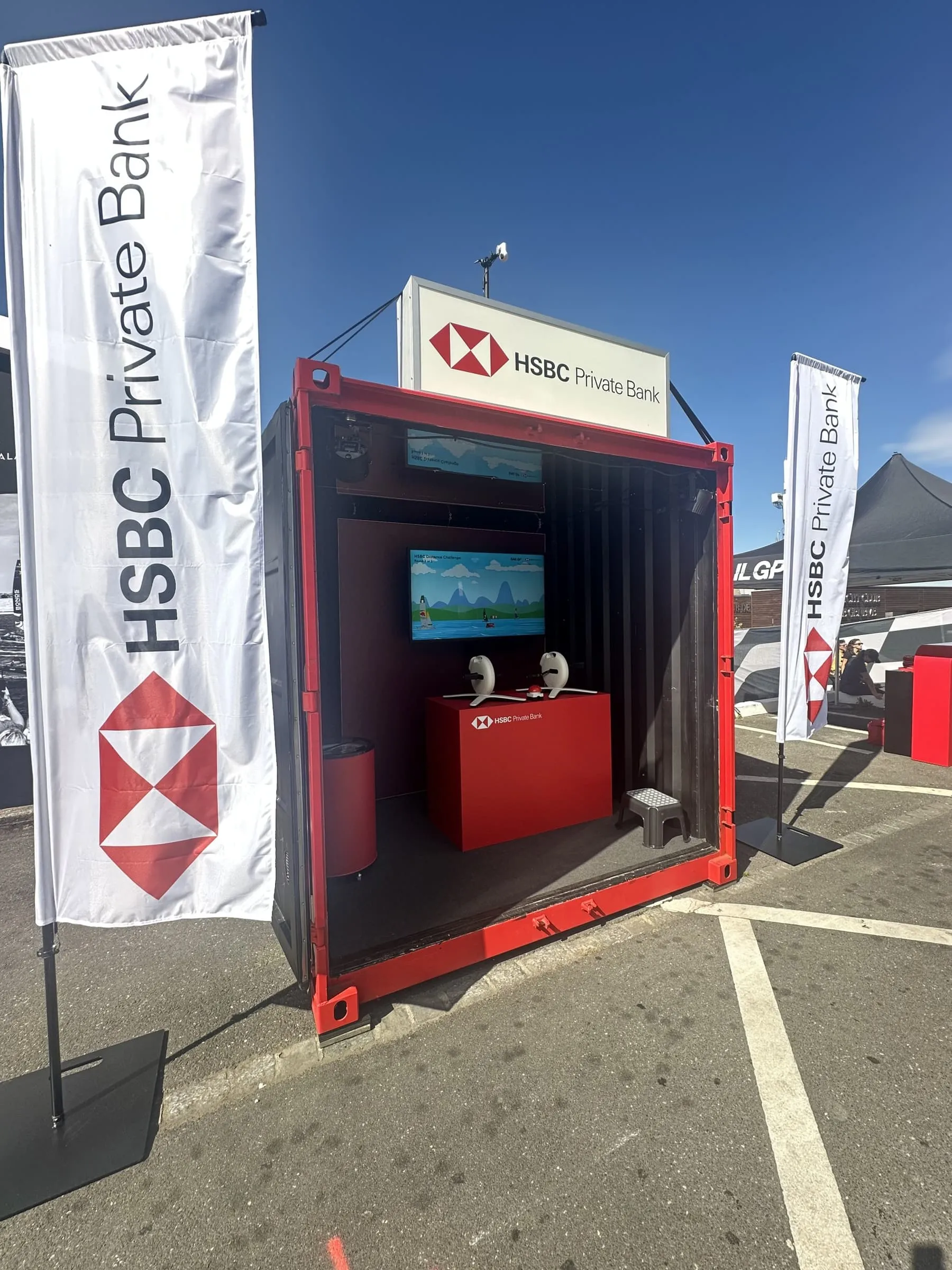 Red HSBC container with an illuminated sign, screen and two pedal trainers, flanked by HSBC Private Bank flags