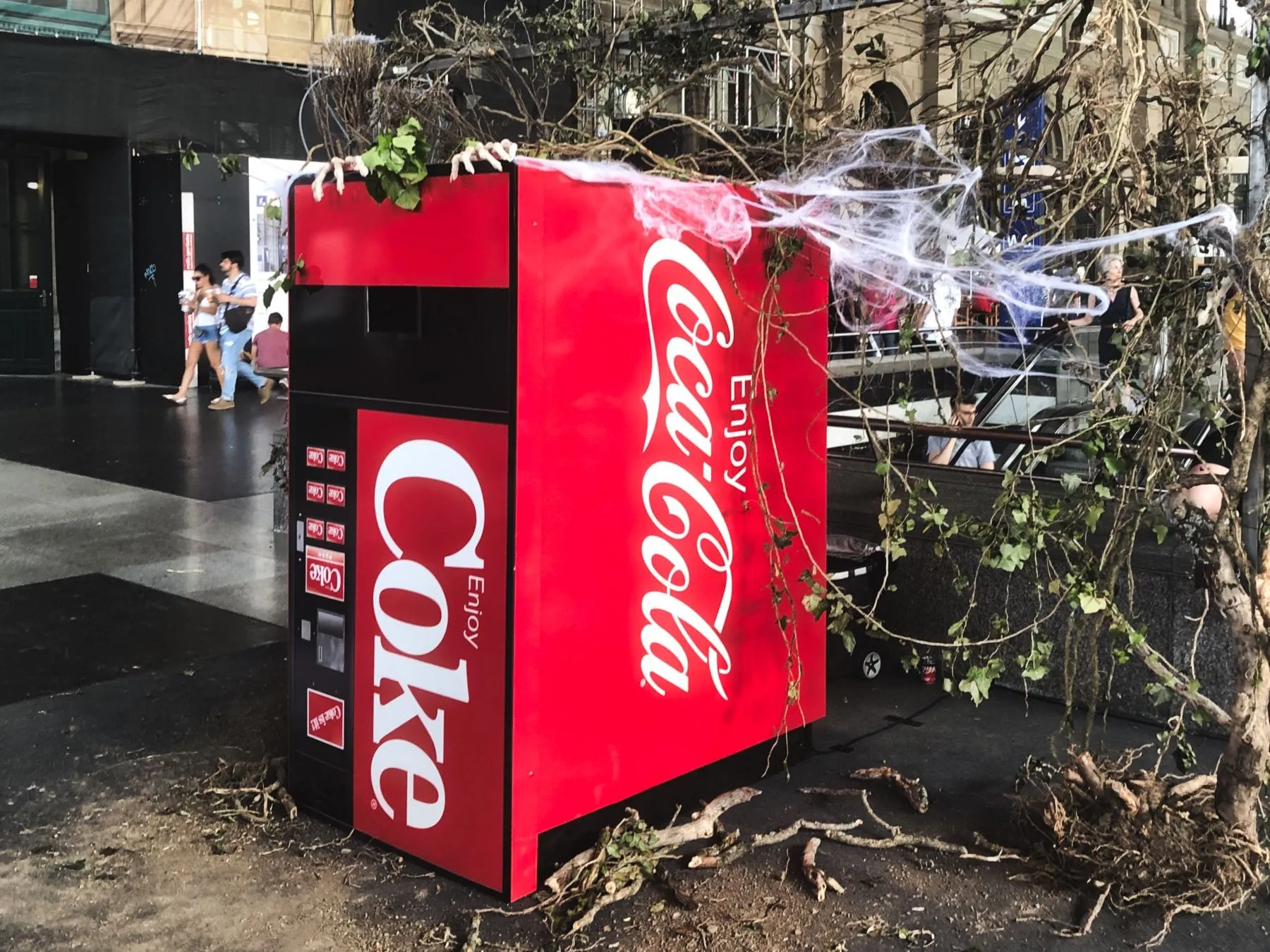 Upside-down red Coca-Cola machine with cobwebs, branches and skeleton hands outside Zürich main station