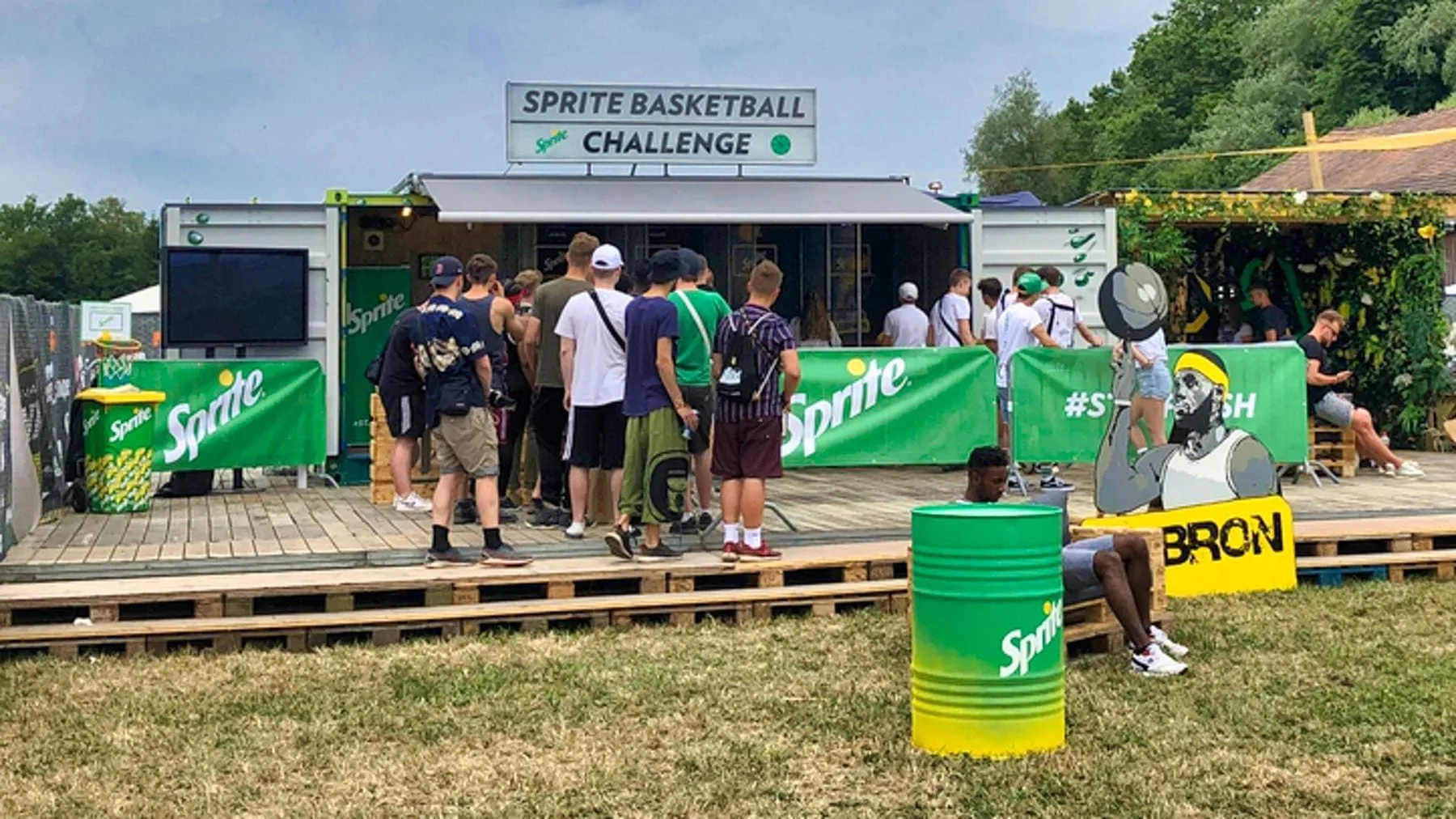 Sprite-Container mit Leuchtschild «Sprite Basketball Challenge», wartende Jugendliche und LeBron-Aufsteller auf Palettenboden