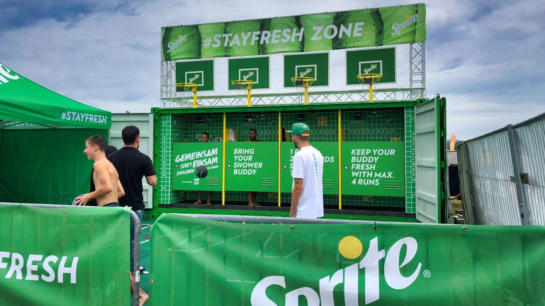 Green Sprite container of the Stayfresh Zone with four shower cabins and basketball hoops, visitors standing in front