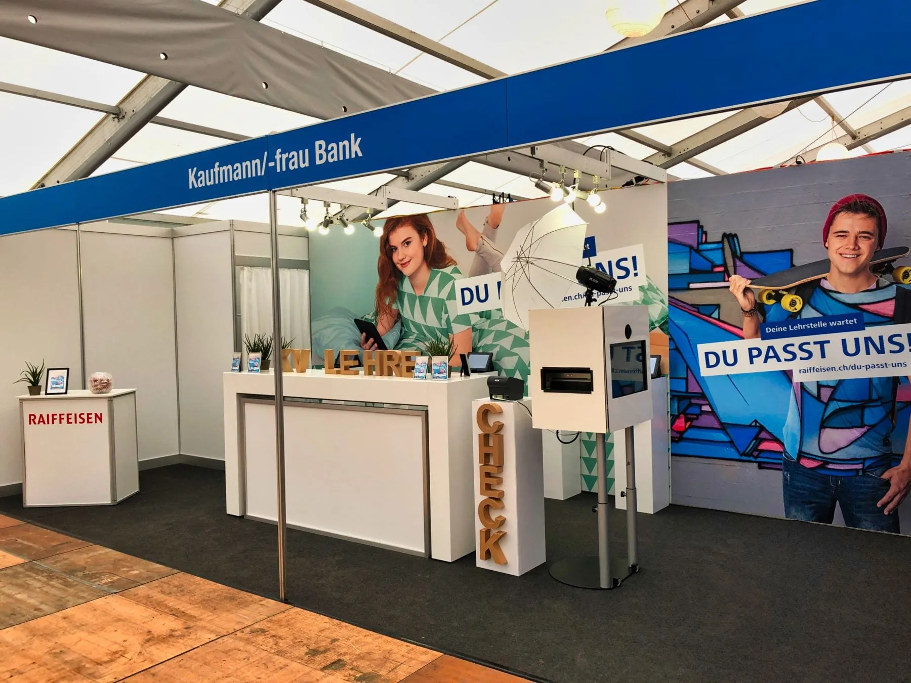 Messestand «Kaufmann/-frau Bank» von Raiffeisen mit Tresen, Fotostation, Schirm und Kampagnenwänden