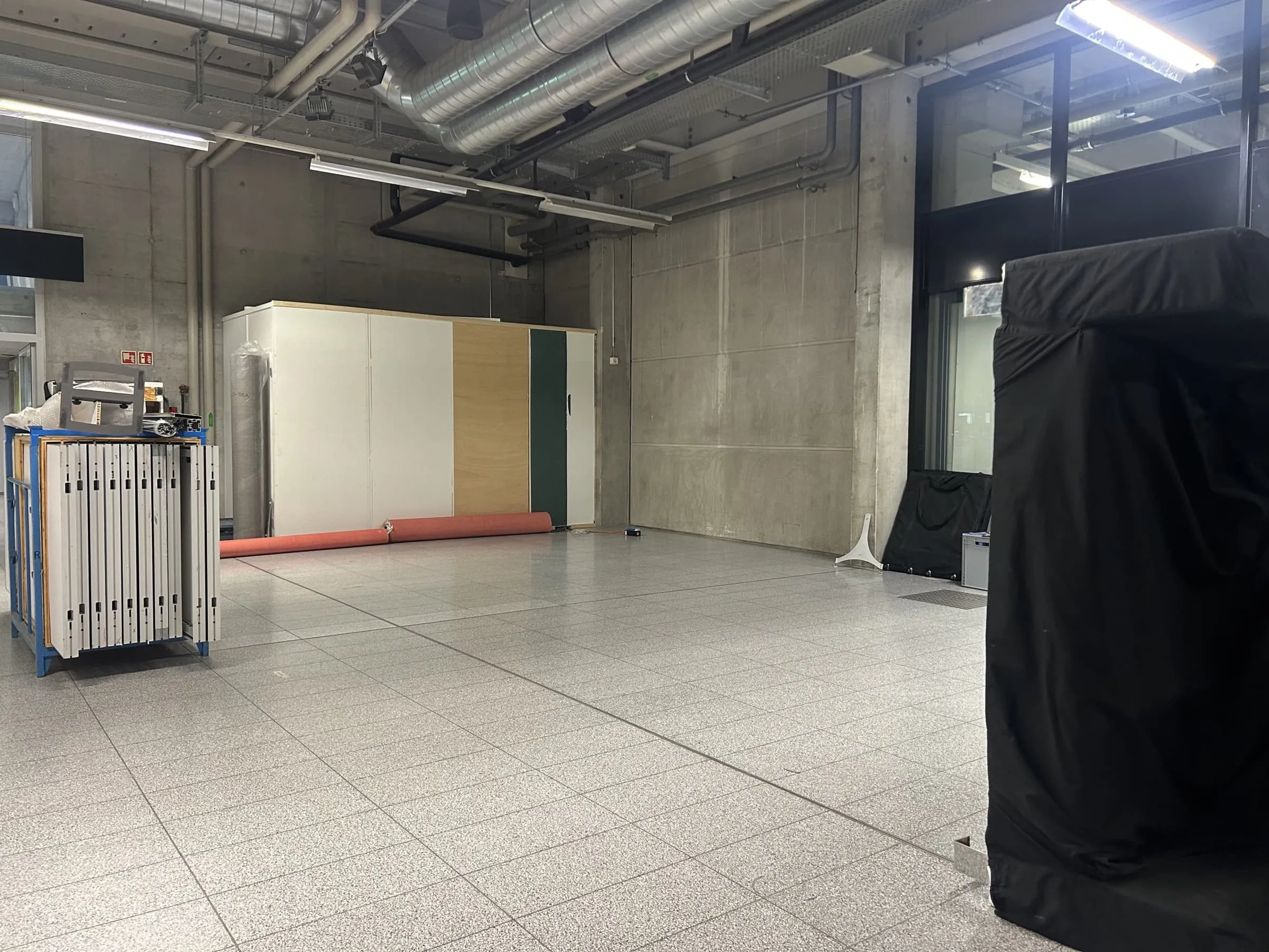 Leere Standfläche in der Messehalle mit Wandelementen, Teppichrolle und Transportwagen