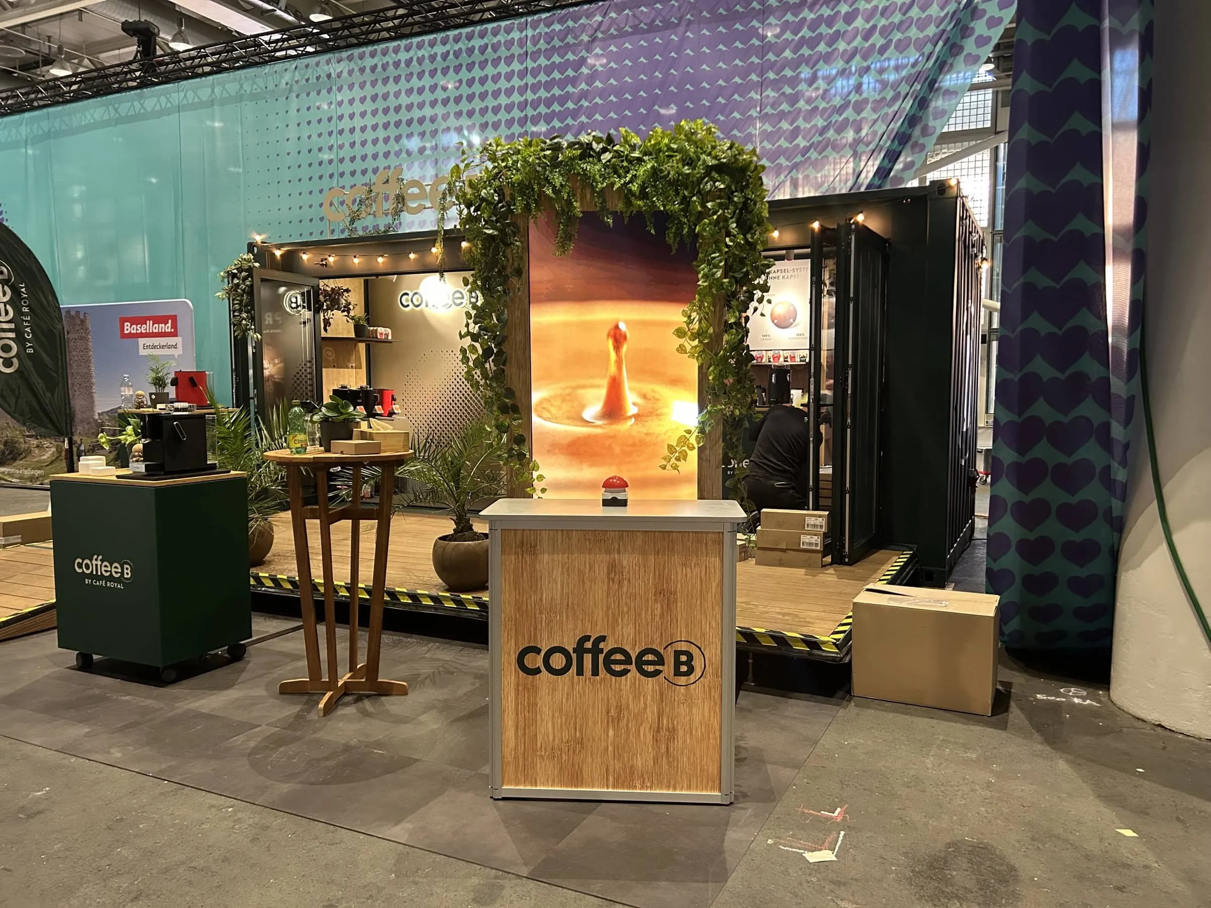 Coffee B stand at Eurovision with a Glücksrad counter, buzzer, planted screen frame and a container with string lights