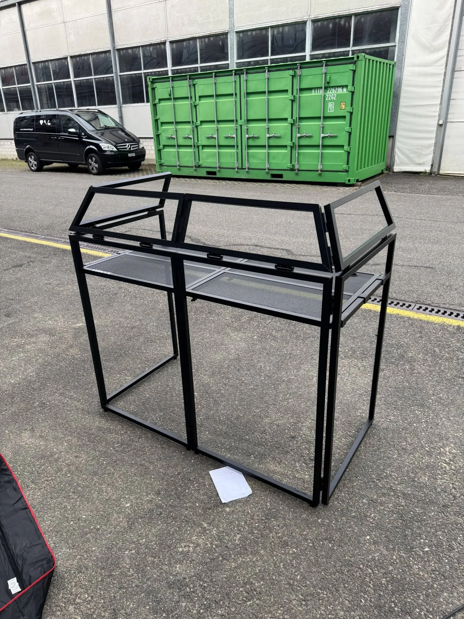 Schwarzes Falttheken-Gestell aus Metall vor der Werkstatt, dahinter ein grüner Container und der made-Bus