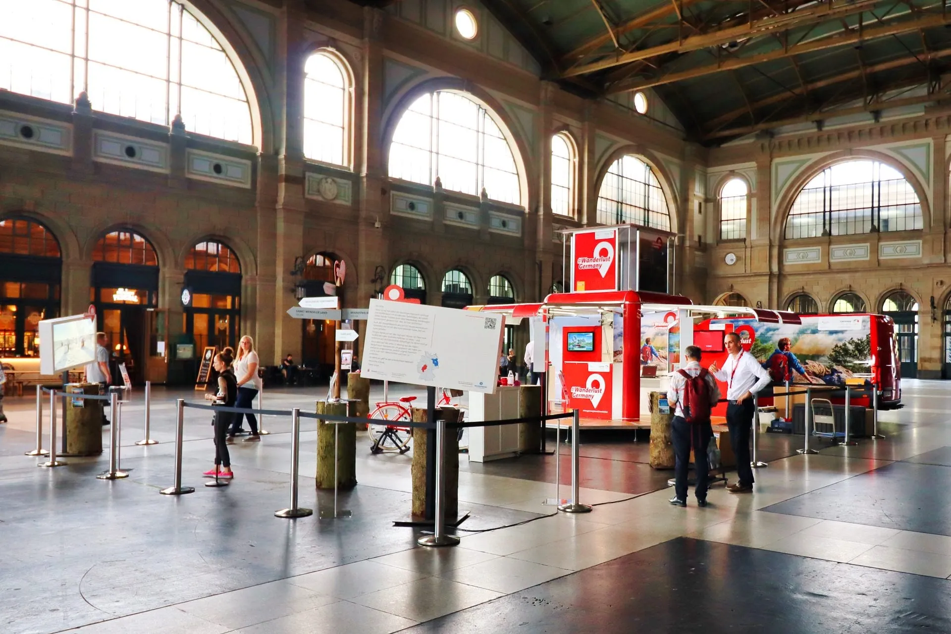 Übersicht des Stands in der Bahnhofshalle Zürich: roter Cube, Riesenpostkarten, Baumstämme und Bildschirme