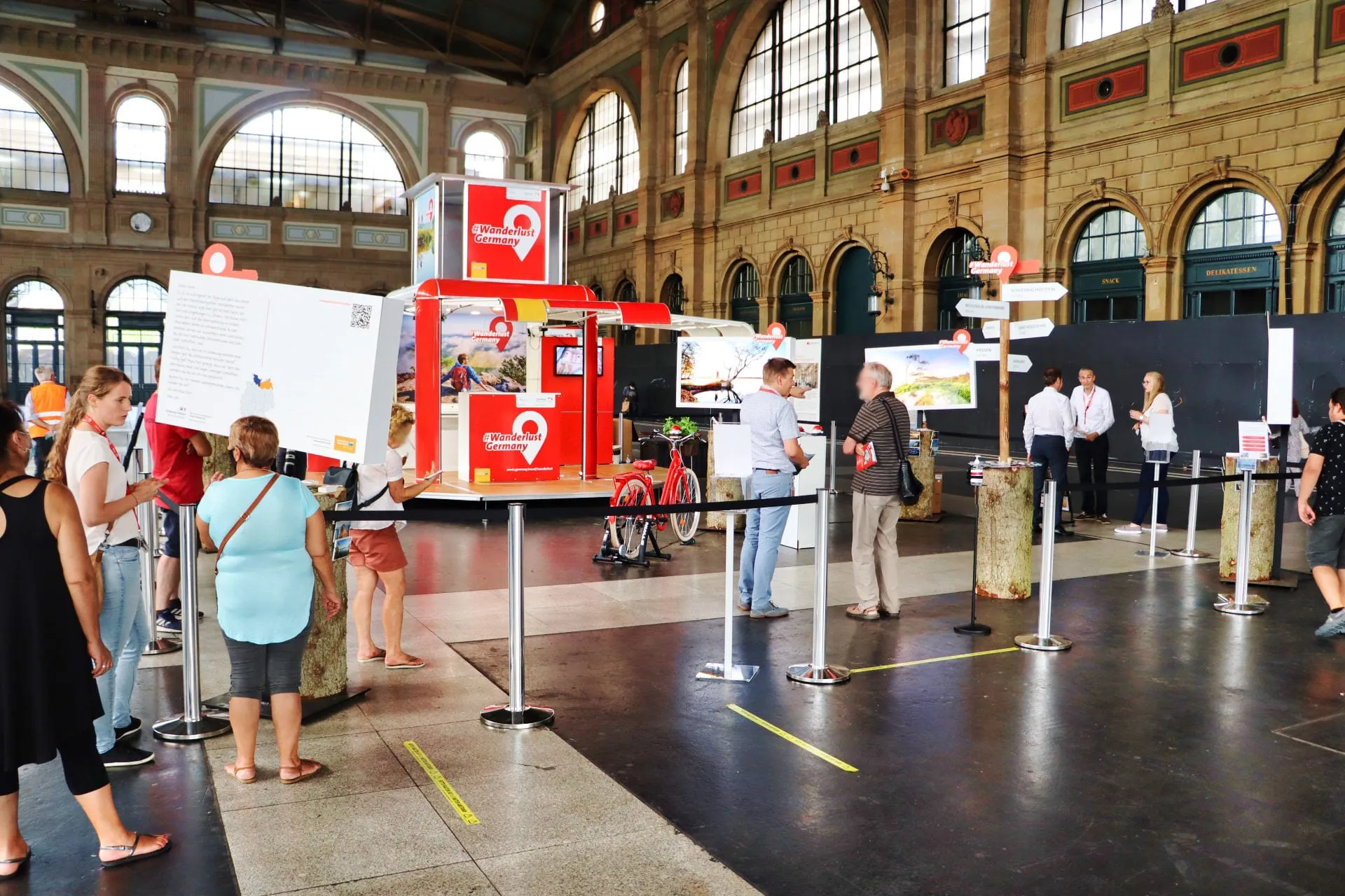 Besuchende vor der Riesenpostkarte und dem roten Cube, Bildschirme mit Ferienbildern und Absperrbänder
